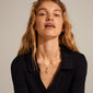 Woman with long blonde hair wearing the DAGMAR pendant necklace, a gold-plated Pilgrim piece featuring the iconic Dagmar Cross, styled over a black shirt.