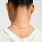 Person wearing the DAGMAR pendant necklace gold-plated with a delicate drop-chain detail, elegantly draped on the back of the neck over a white top.