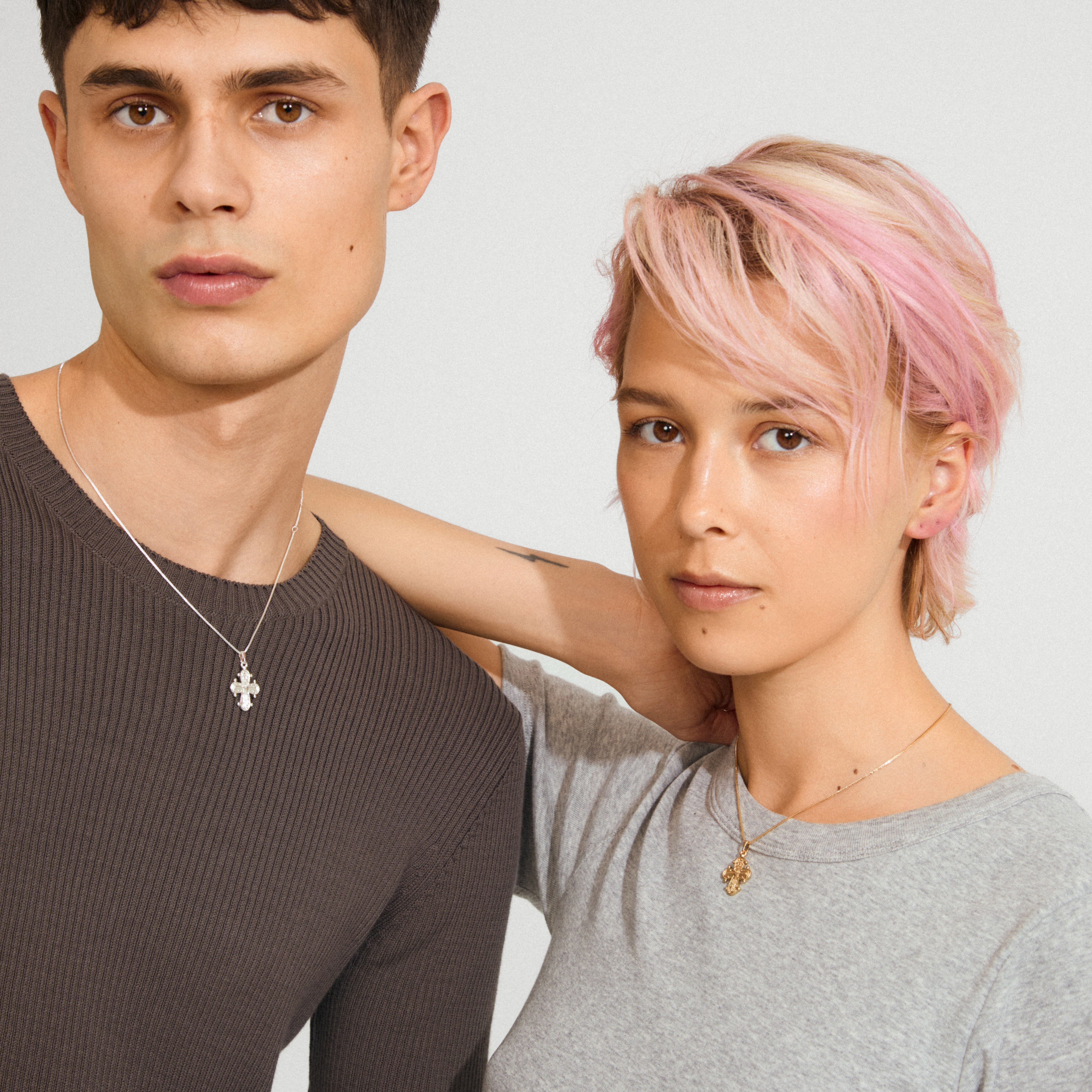 Two young adults wearing Pilgrim's DAGMAR pendant necklaces—silver on the left, gold on the right—styled in a minimalist, contemporary fashion.