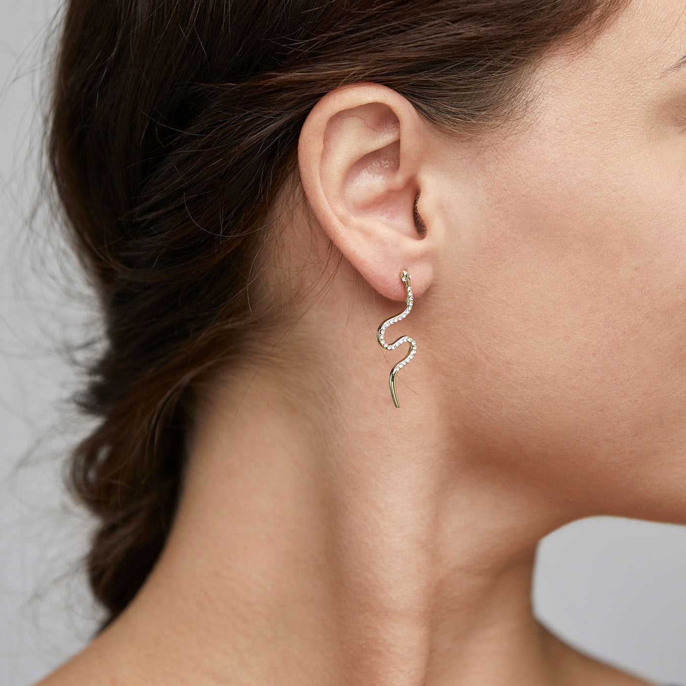DAGNY crystal earrings gold-plated, featuring gold-plated serpents adorned with crystals, elegantly hanging and coiling from a woman's earlobe.