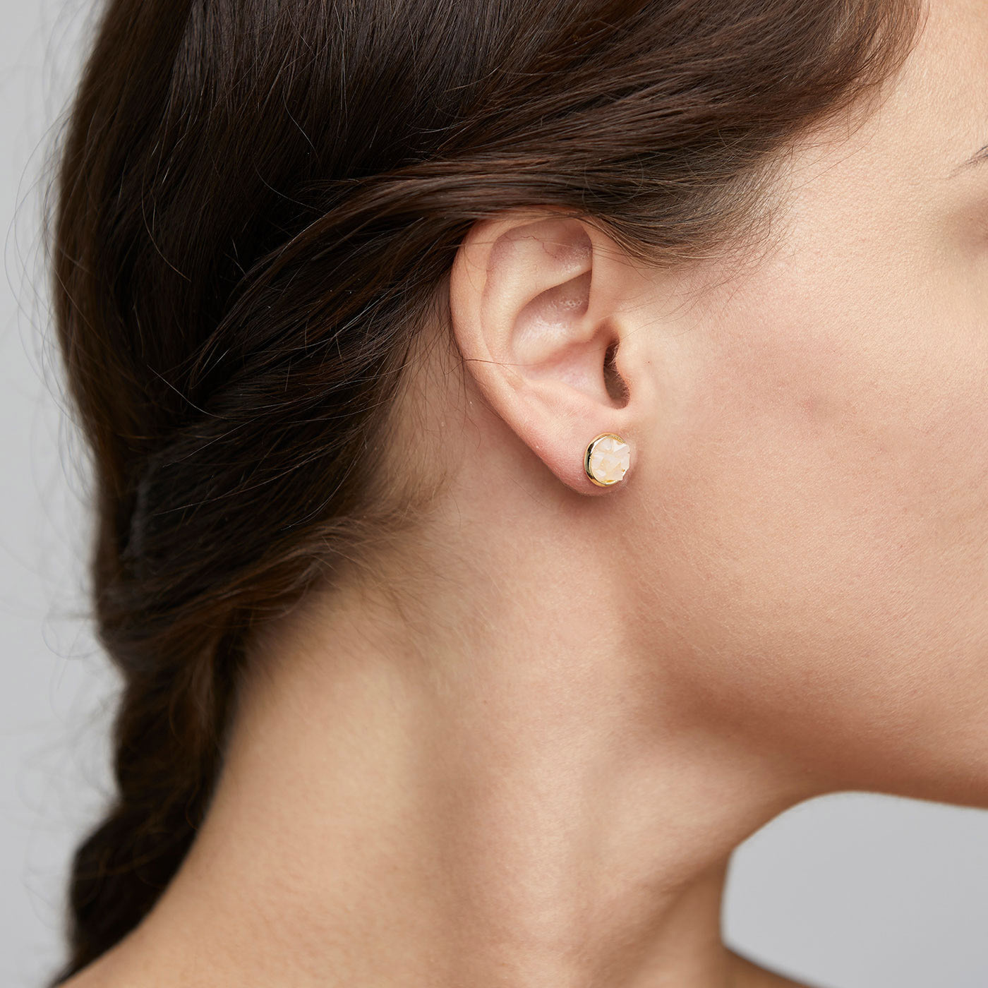 Close-up of a woman's ear wearing JOSEFINE earrings, featuring gold-plated studs with a rustic pink stone, combining edgy texture and elegant shine.
