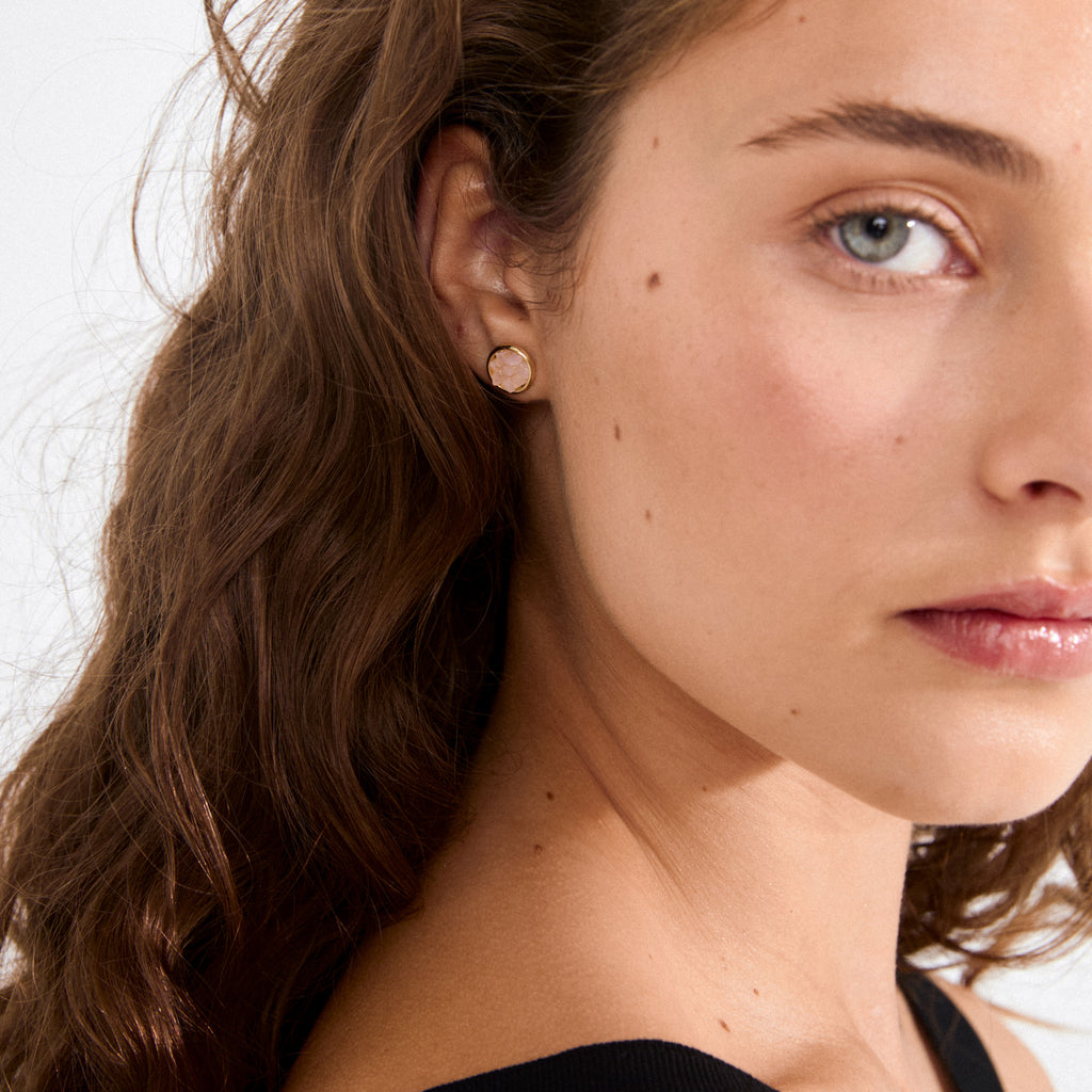 JOSEFINE earrings gold-plated feature a rustic pink stone in a smooth gold bezel, exuding edgy elegance on a young woman's ear.