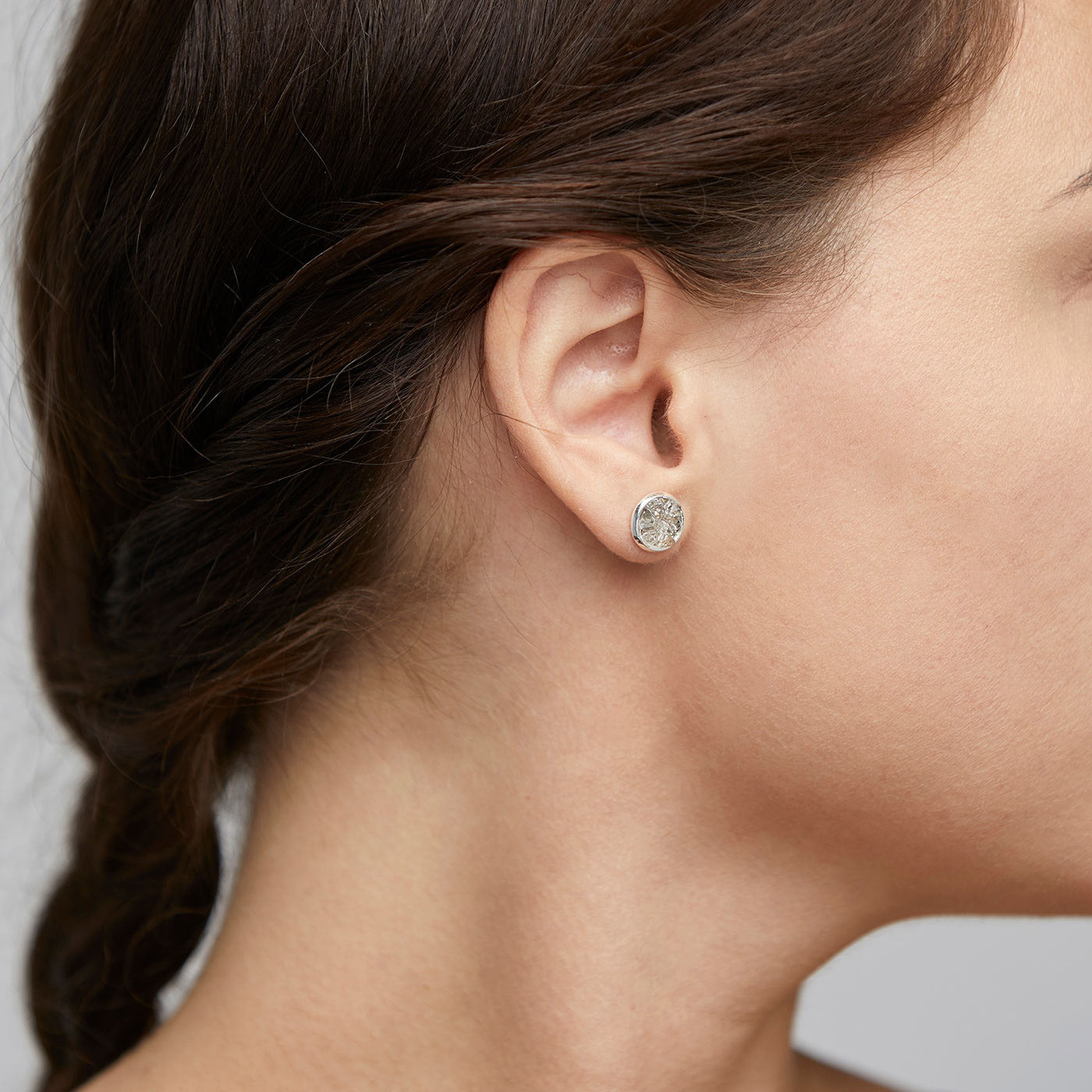 Close-up of a woman's ear wearing JOSEFINE silver-plated earrings, featuring a rustic grey stone with a shiny round setting, blending edgy and elegant styles.