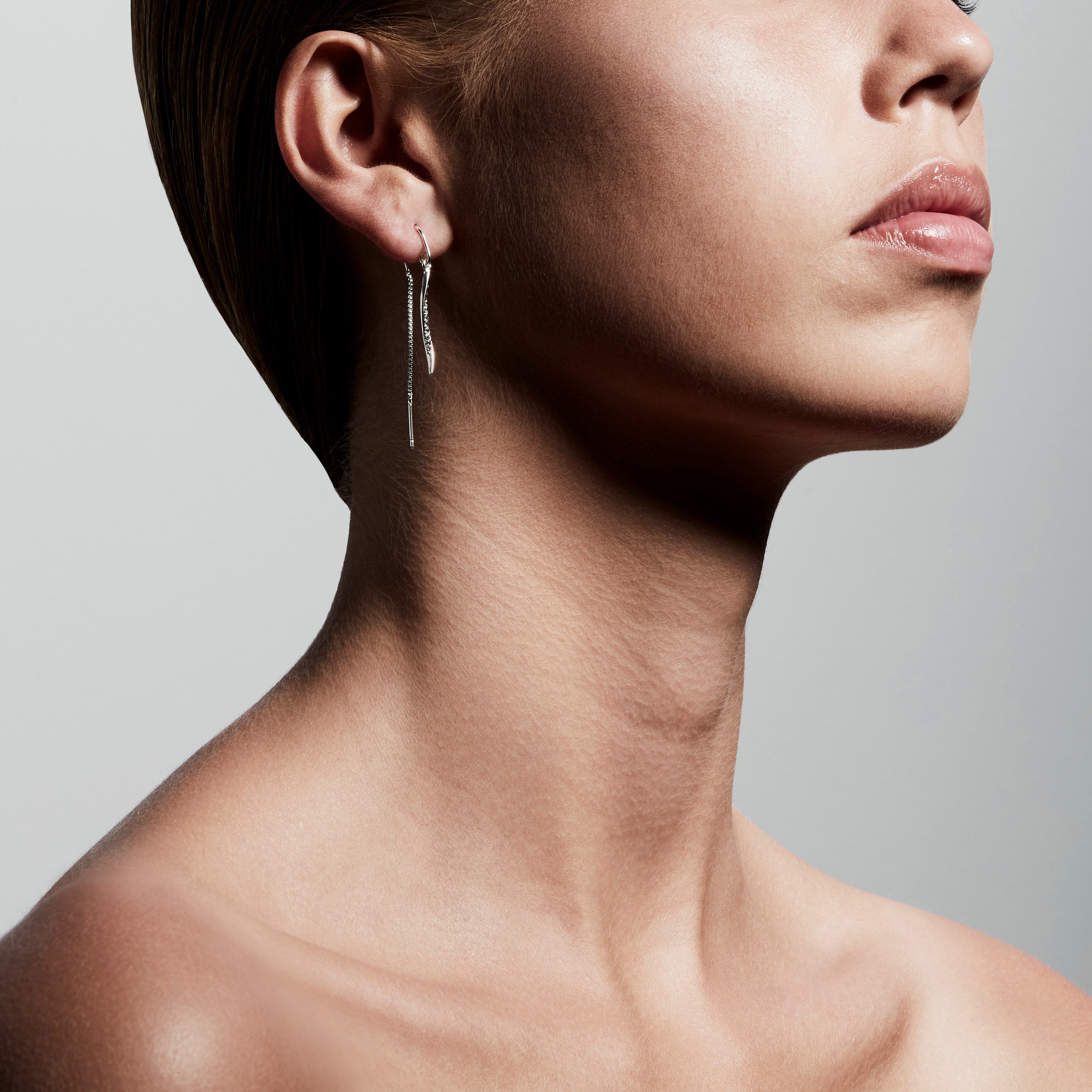 MALIA silver-plated earrings featuring Preciosa crystals, chains, and pendants, worn by a woman with a short haircut and matching necklace.