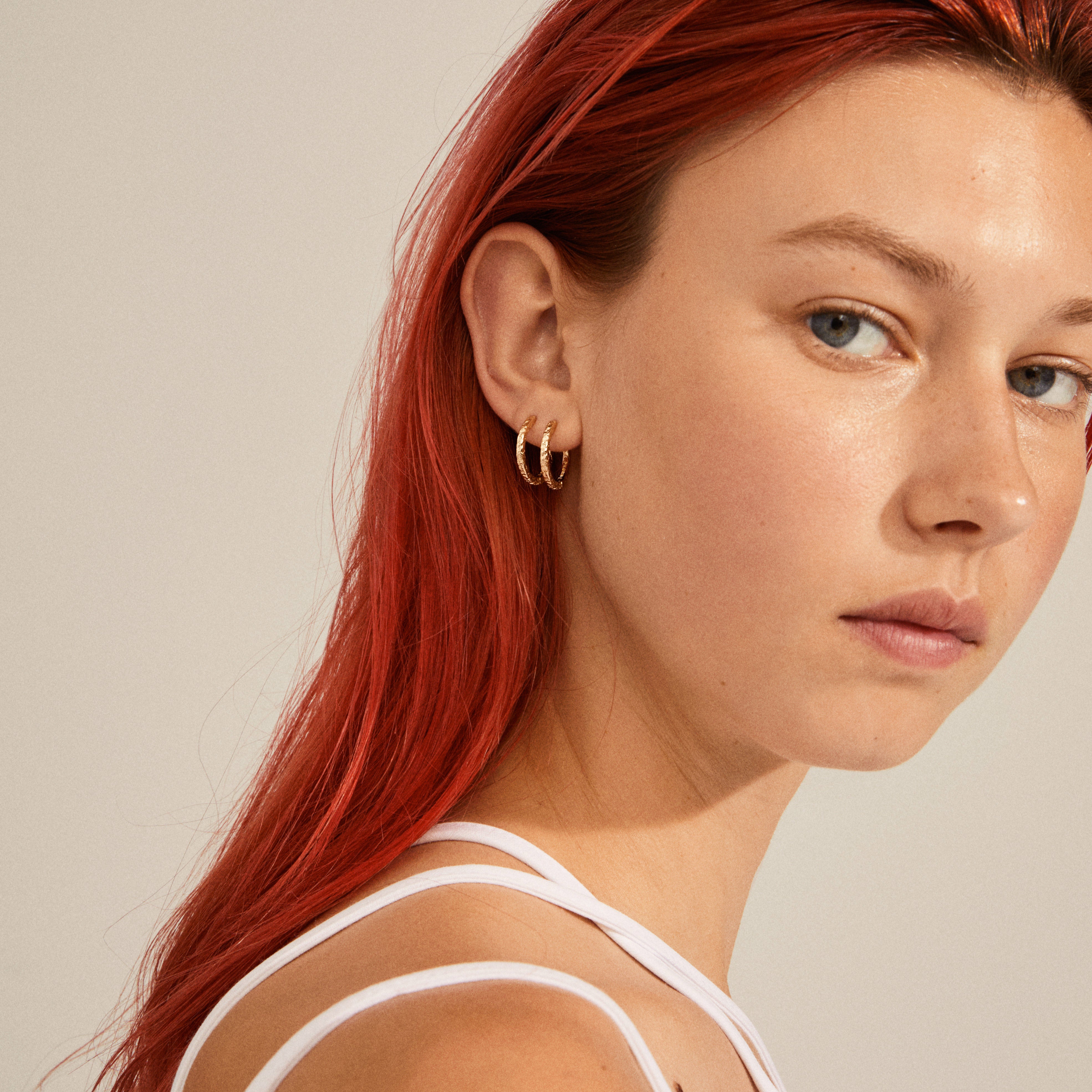 Gold-plated ELANOR rustic texture hoop earrings on a woman with red hair, showcasing their organic design and shiny finish, reflecting Pilgrim's Scandinavian style.
