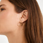 Close-up of a person wearing ELANOR rustic texture gold-plated hoop earrings by Pilgrim, featuring one textured and one smooth small hoop against a plain background.