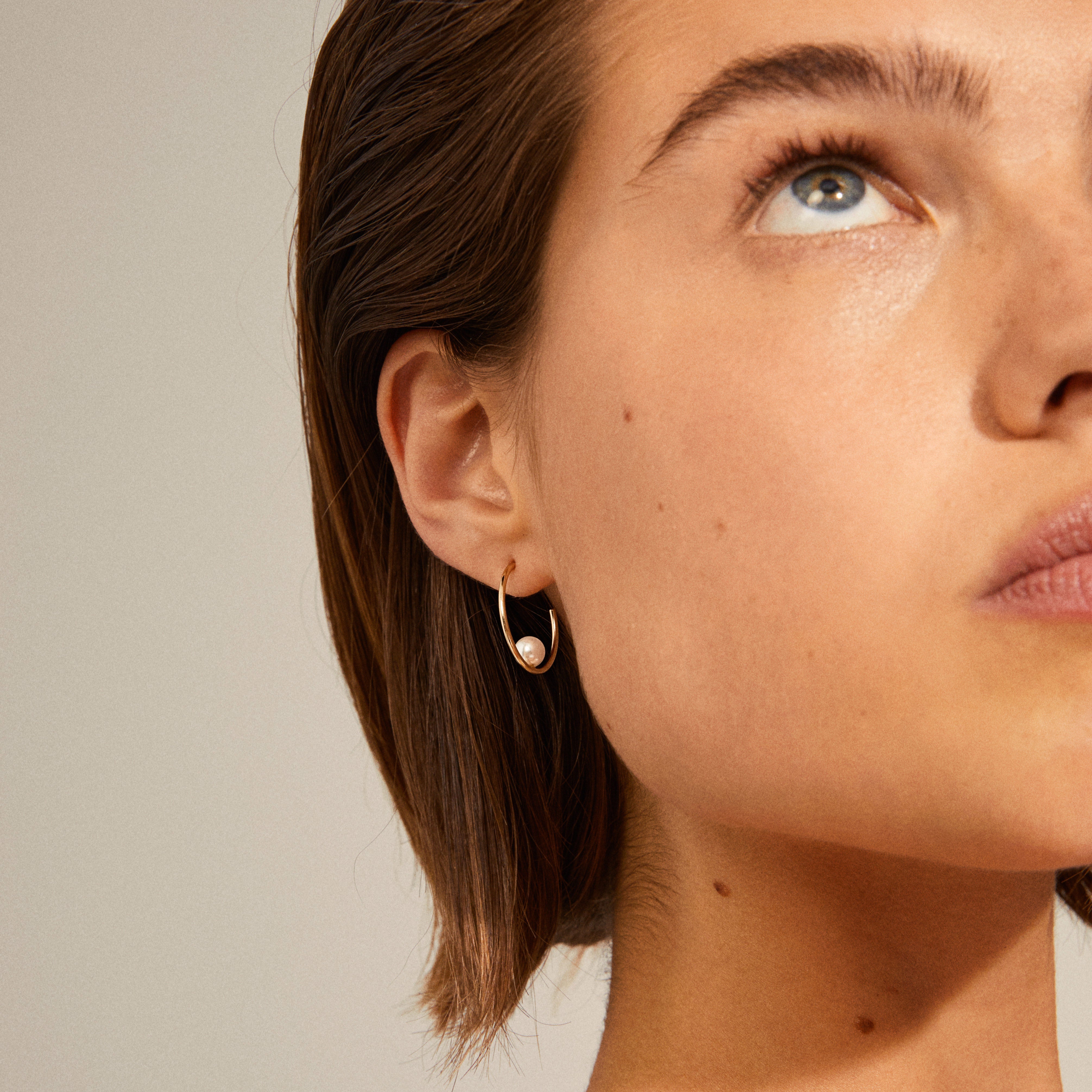 Close-up of a woman wearing Pilgrim's ELINE pearl hoop earrings, gold-plated with a white pearl, showcasing their elegant and stylish design.