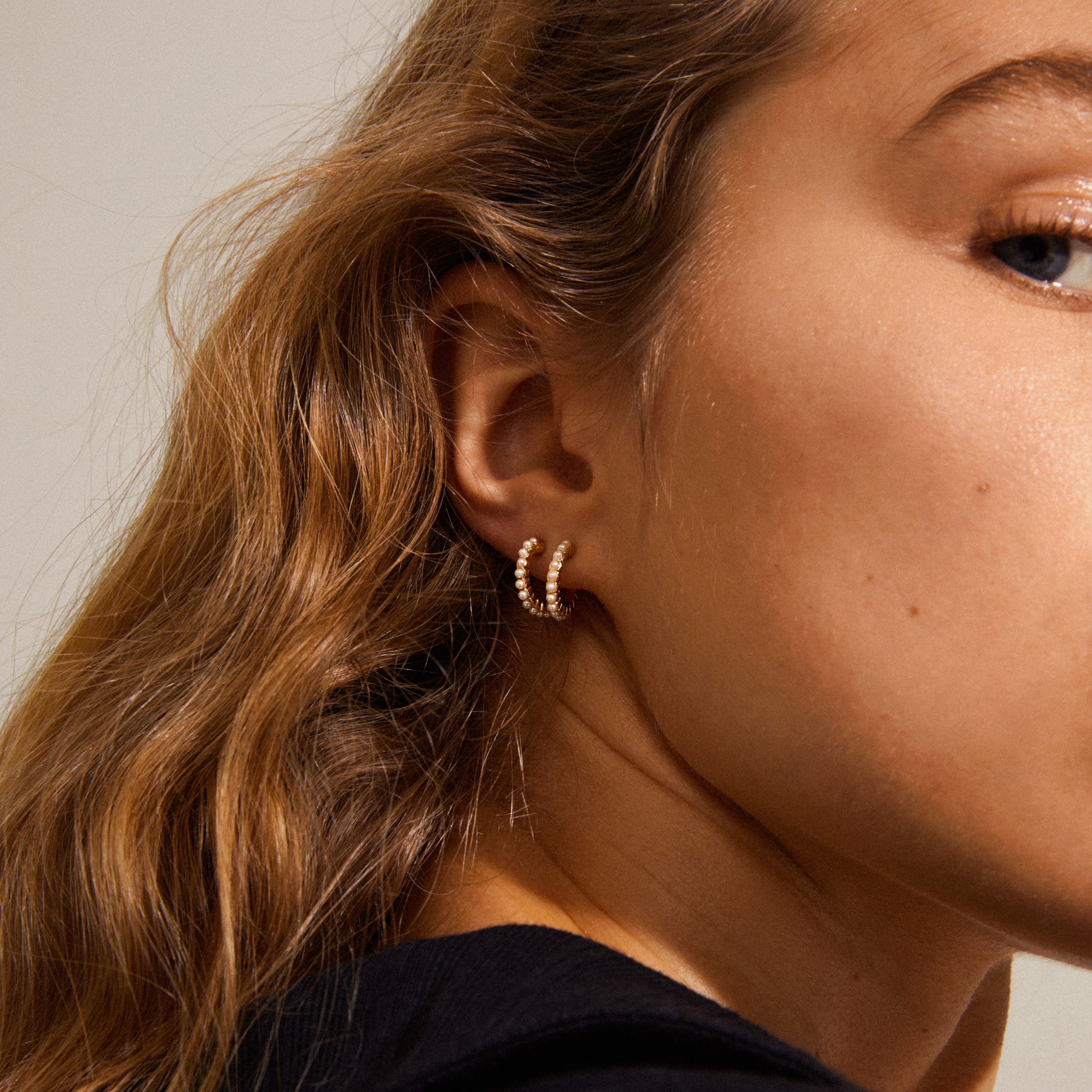 EKTA pearl huggie hoop earrings gold-plated, featuring a close-up of a woman's ear adorned with the elegant, pearl-accented gold hoops from Pilgrim's Classics collection.