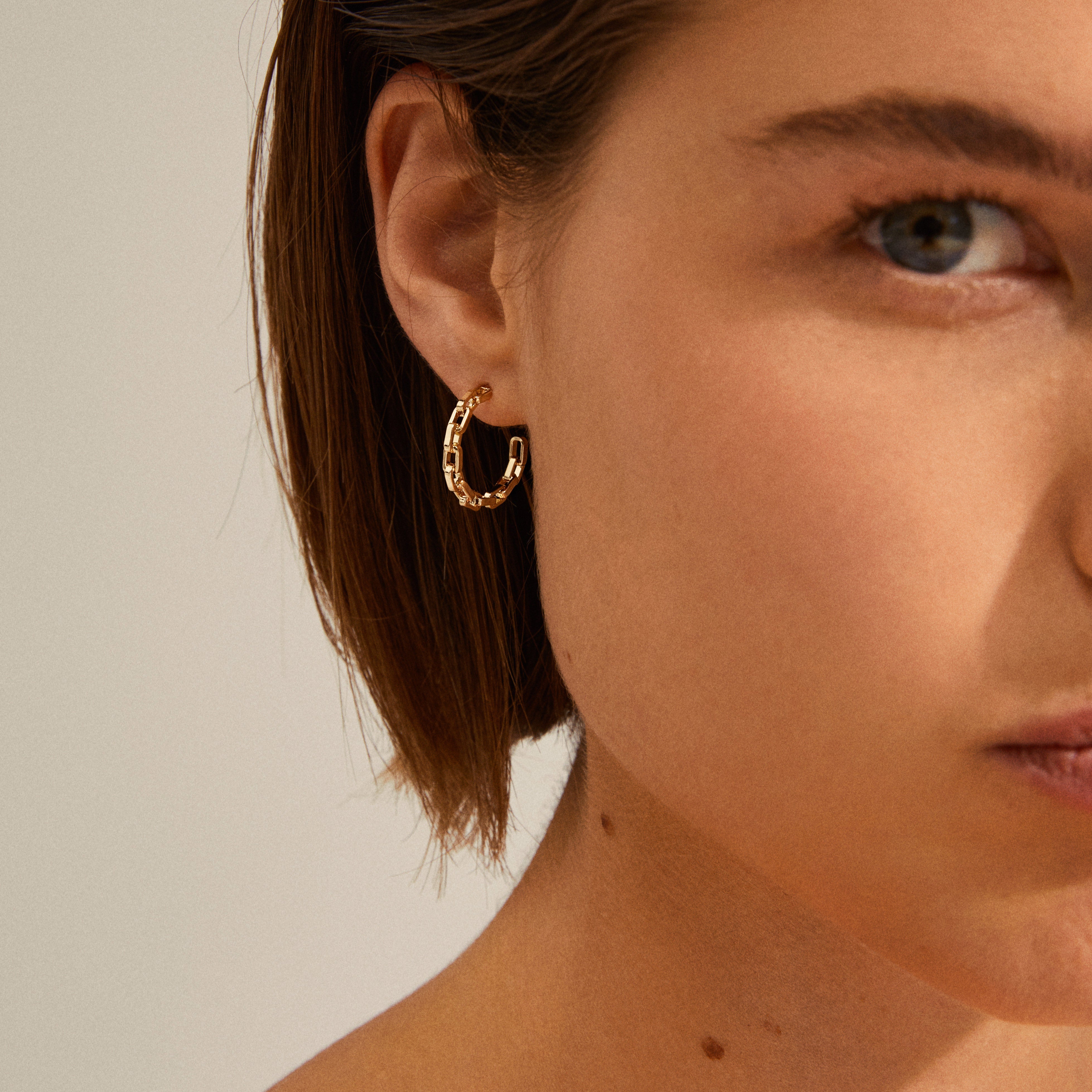 EIRA cable chain hoop earrings gold-plated, featuring a trendy, robust design inspired by cable chains, elegantly adorn a woman's ear in this close-up shot.