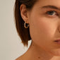 EIRA cable chain hoop earrings gold-plated, featuring a trendy, robust design inspired by cable chains, elegantly adorn a woman's ear in this close-up shot.