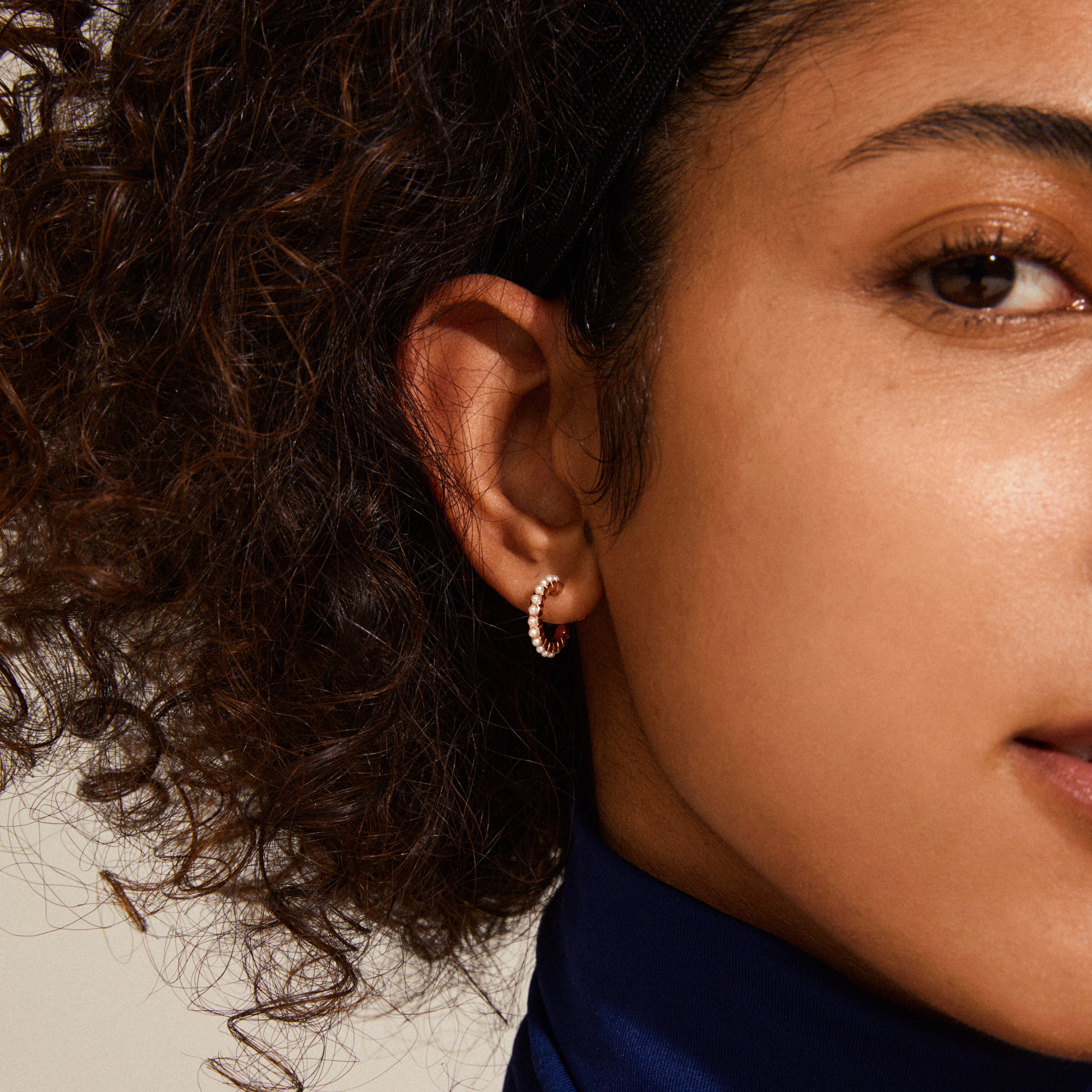 EKTA pearl huggie hoop earrings, rose gold-plated, featuring elegant pearls, showcased on a woman's ear for a sophisticated, glam look.
