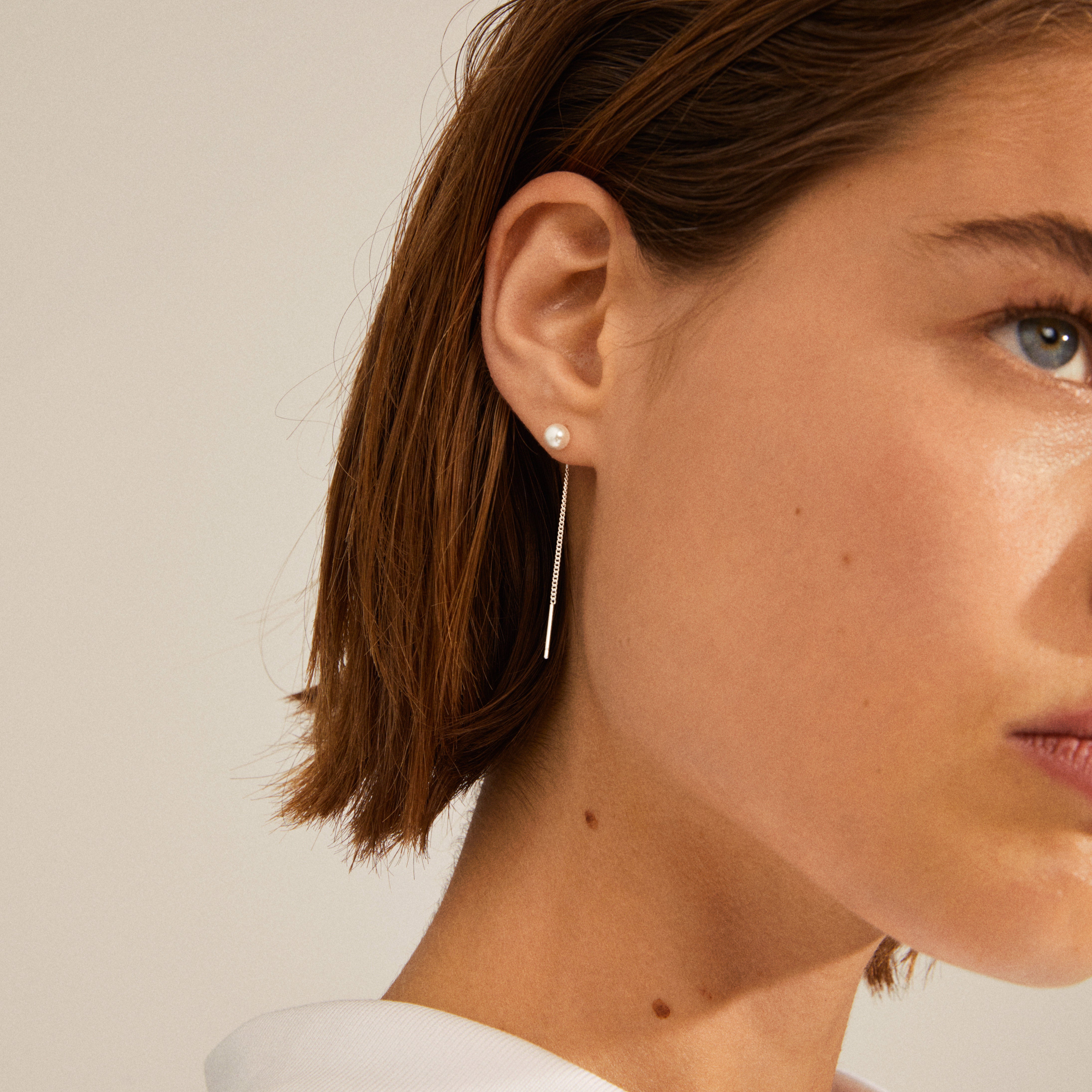 Close-up of a woman wearing silver-plated ELBA long chain pearl earrings, highlighting the elegant pearl stud and delicate chain hanging behind the ear.