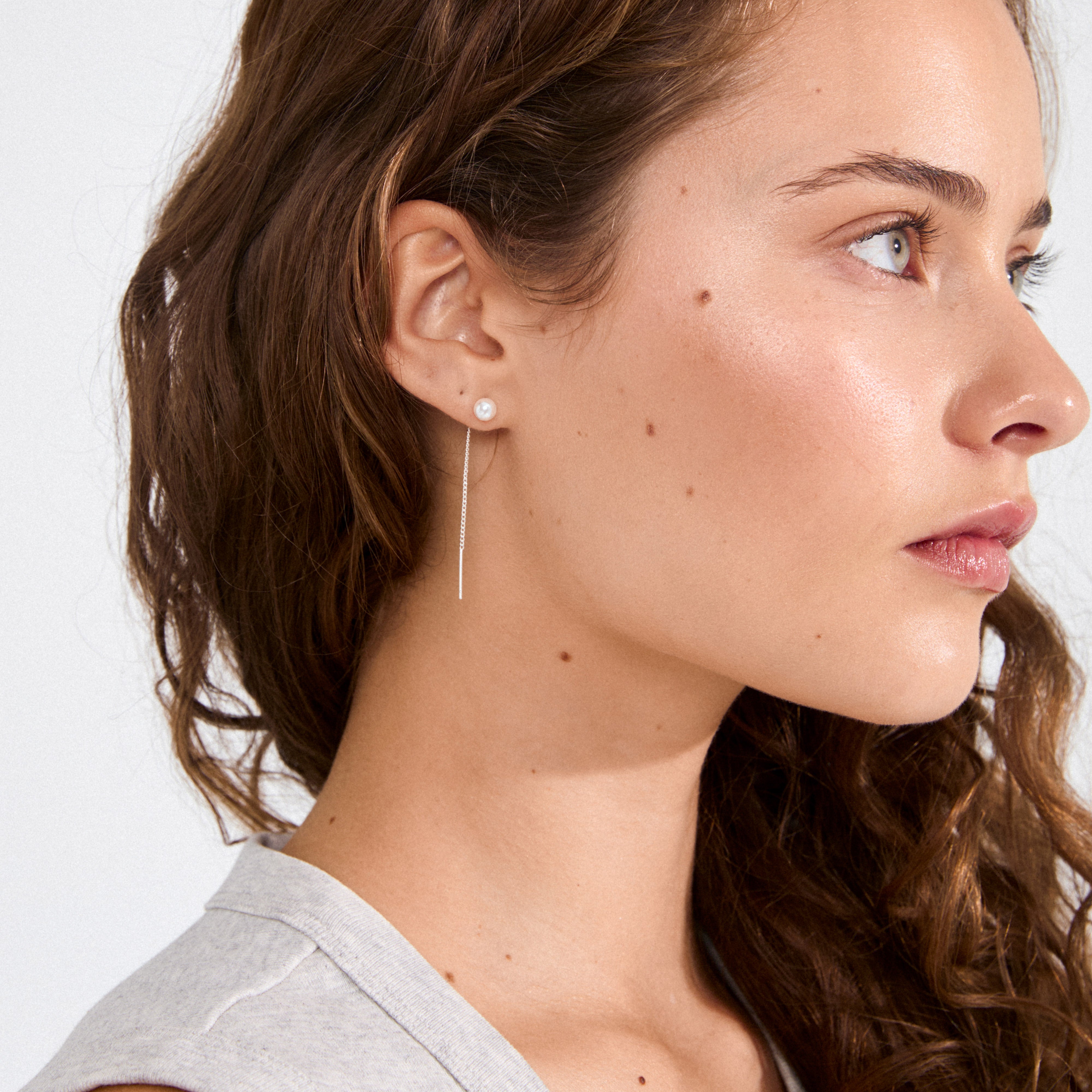 Young woman wears ELBA long chain pearl earrings silver-plated by Pilgrim, featuring a pearl stud and delicate chain drop for a chic, modern look.