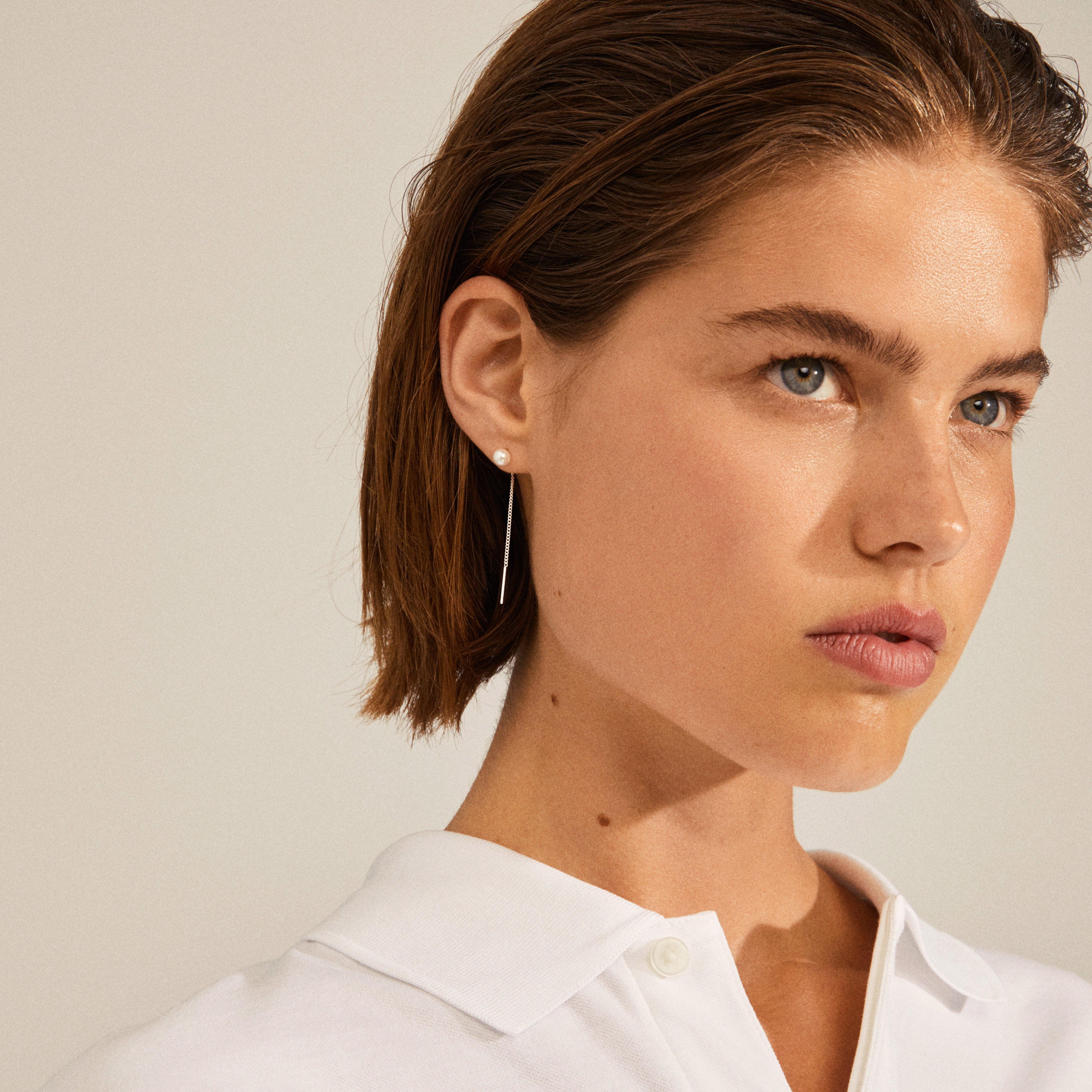 Woman wearing ELBA long chain pearl earrings, silver-plated, showcasing the white pearl stud and delicate chain adding movement and elegance.