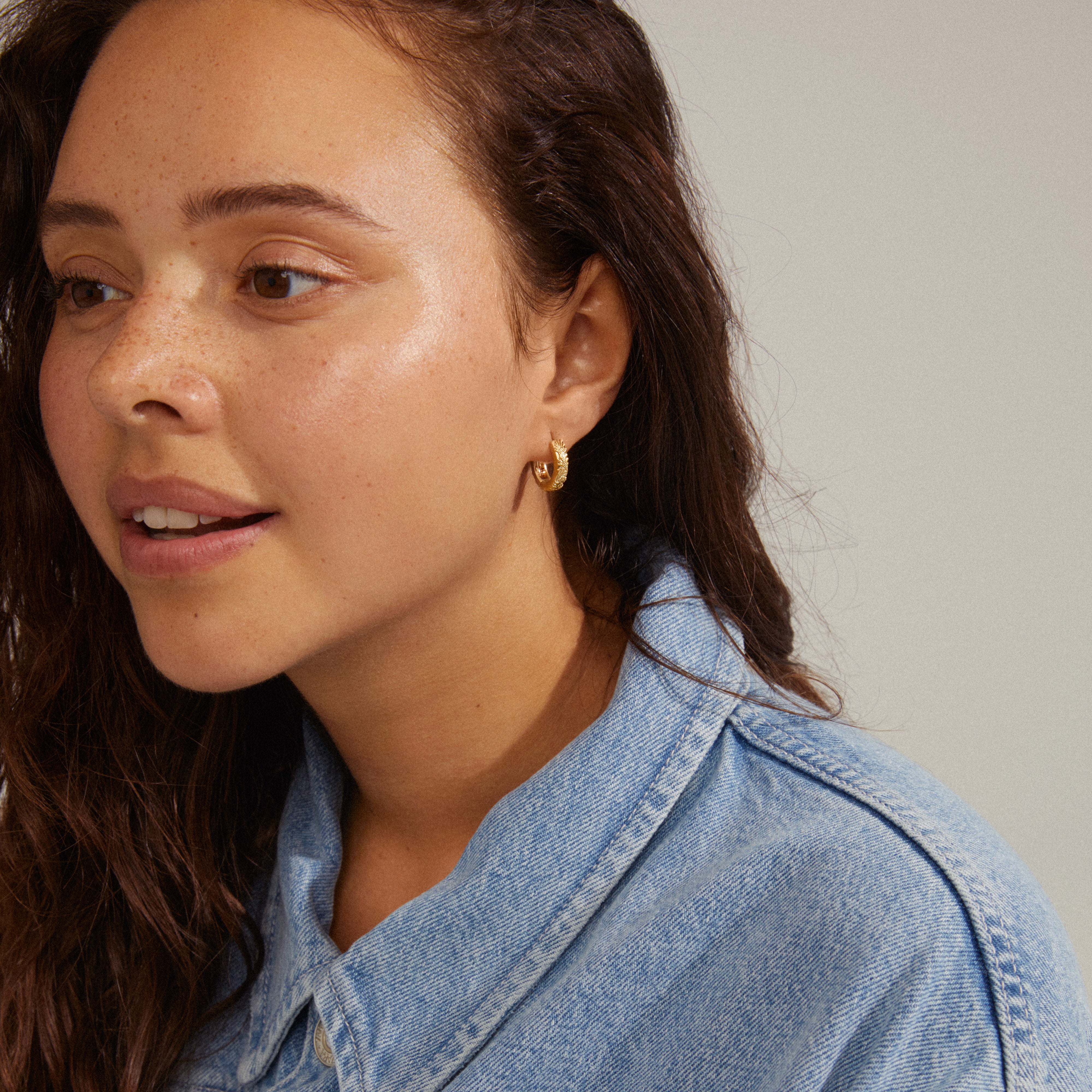 ELFRIDA hoop earrings gold-plated with nature-inspired carvings on a woman, showcasing intricate patterns of flowers and leaves, perfect for a summery style.