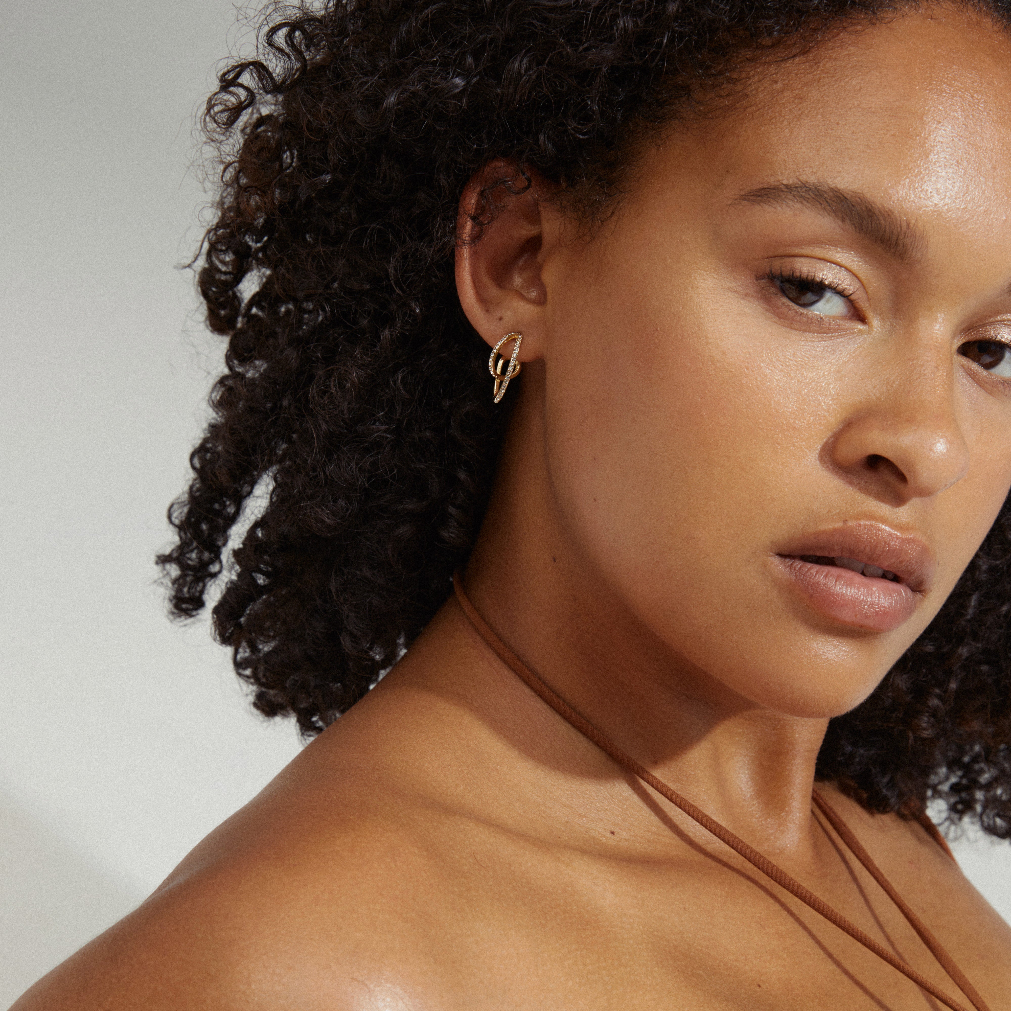 ETTY crystal earrings gold-plated, featuring a stylish silhouette with Preciosa crystals, worn by a woman with curly hair and a necklace. Ideal for glamorous events.