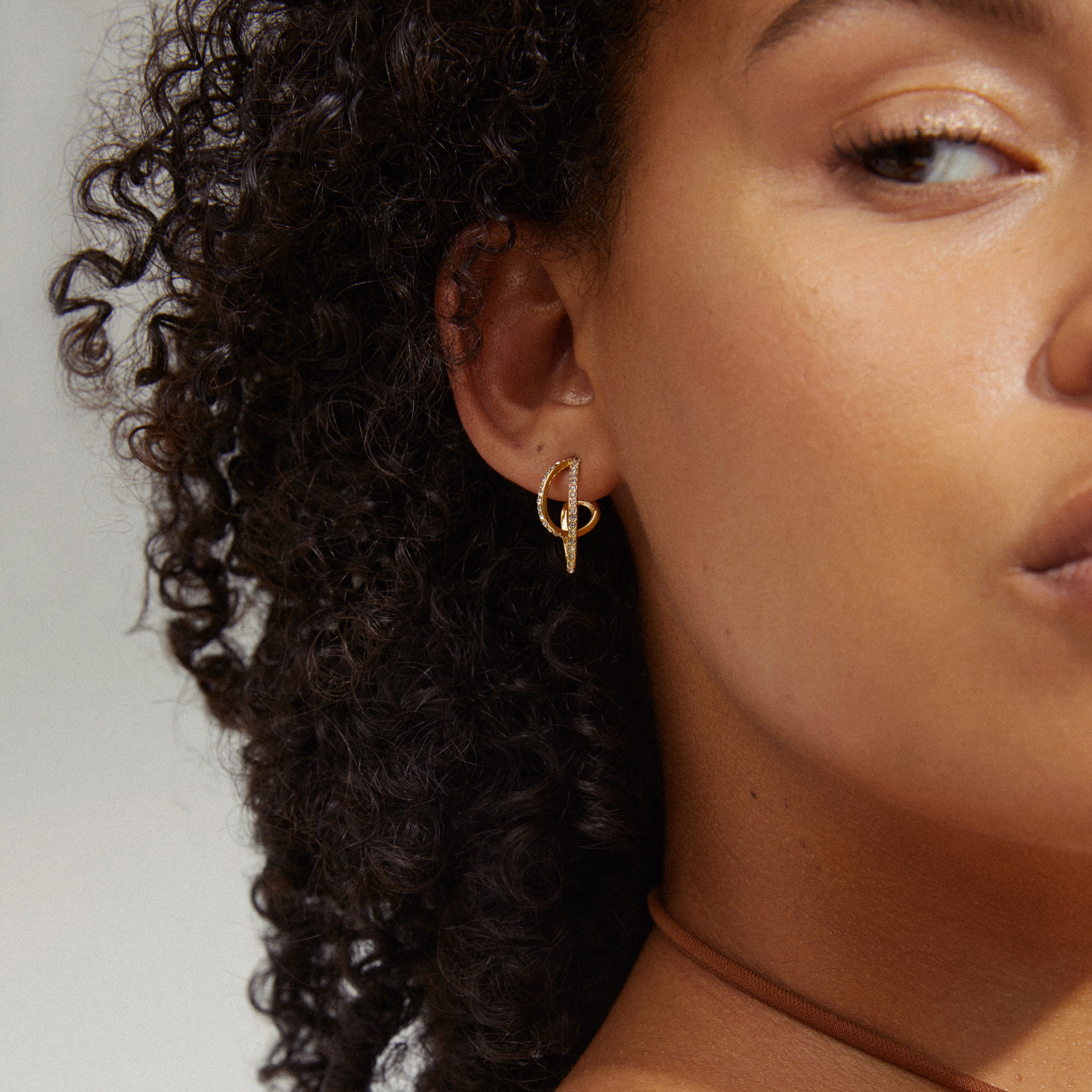Close-up of a woman wearing Pilgrim's gold-plated ETTY crystal earrings, showcasing their elegant hoop design and sparkling Preciosa crystals.