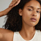 Woman with curly hair wearing EDIL freshwater pearl earrings 3-in-1 set, showcasing various sizes of elegant pearls, reflecting timeless Scandinavian fashion.