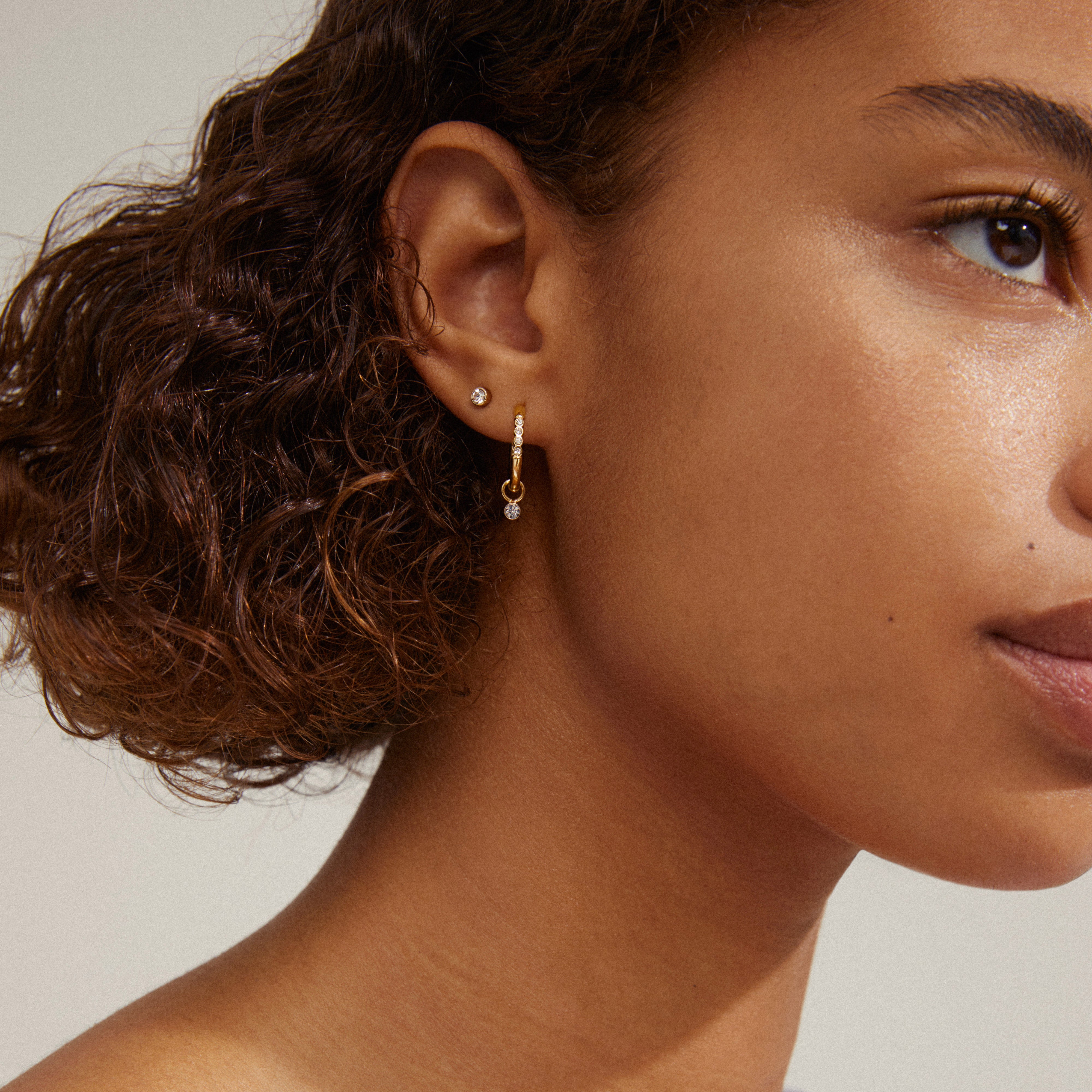 ELNA crystal earrings 2-in-1 set, featuring gold-plated studs and crystal-adorned hoops, beautifully showcased on a woman with curly hair.