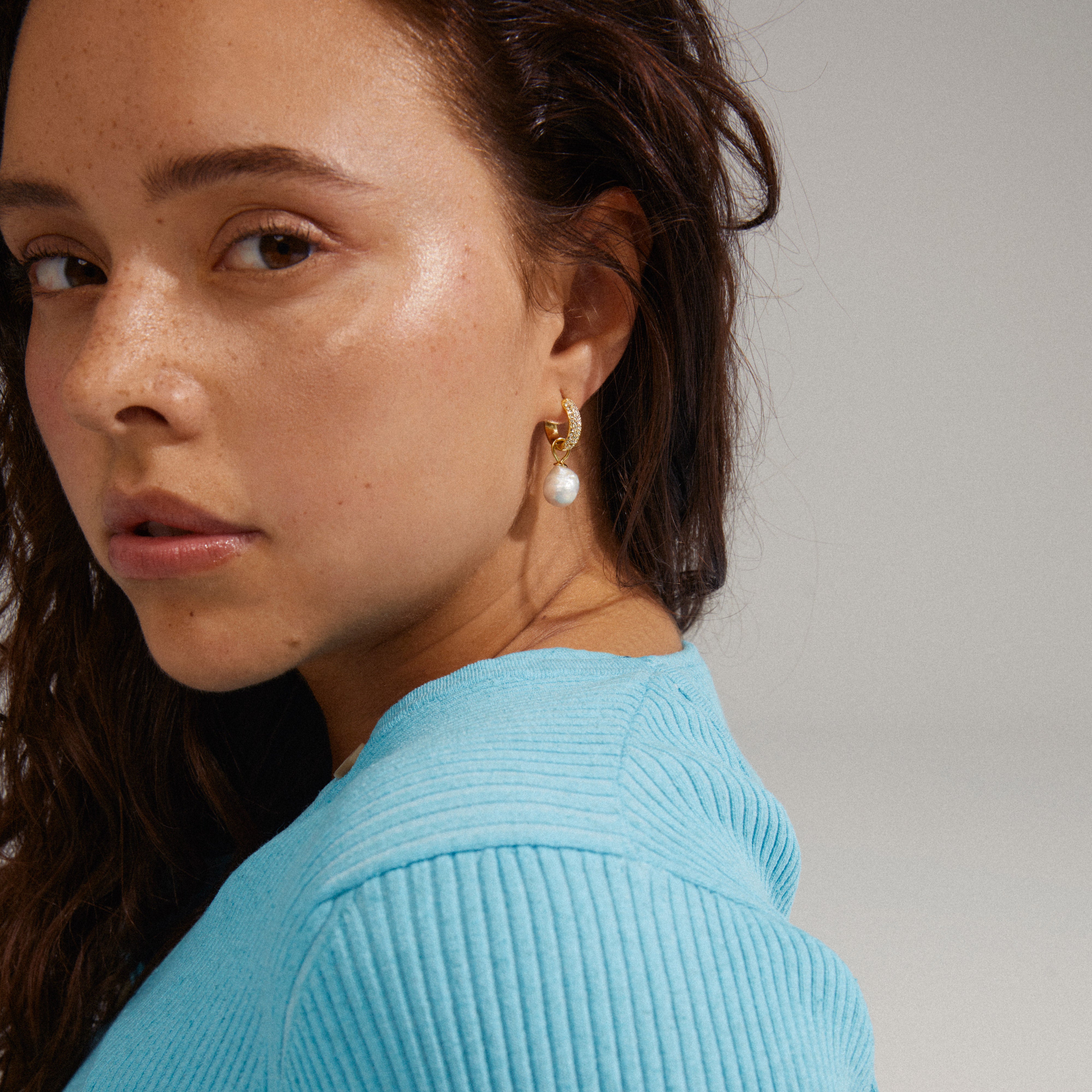 EDELE pearl earrings gold-plated, featuring chunky hoops with Preciosa crystals and detachable pearl pendants, elegantly showcased on a woman wearing a blue shirt.