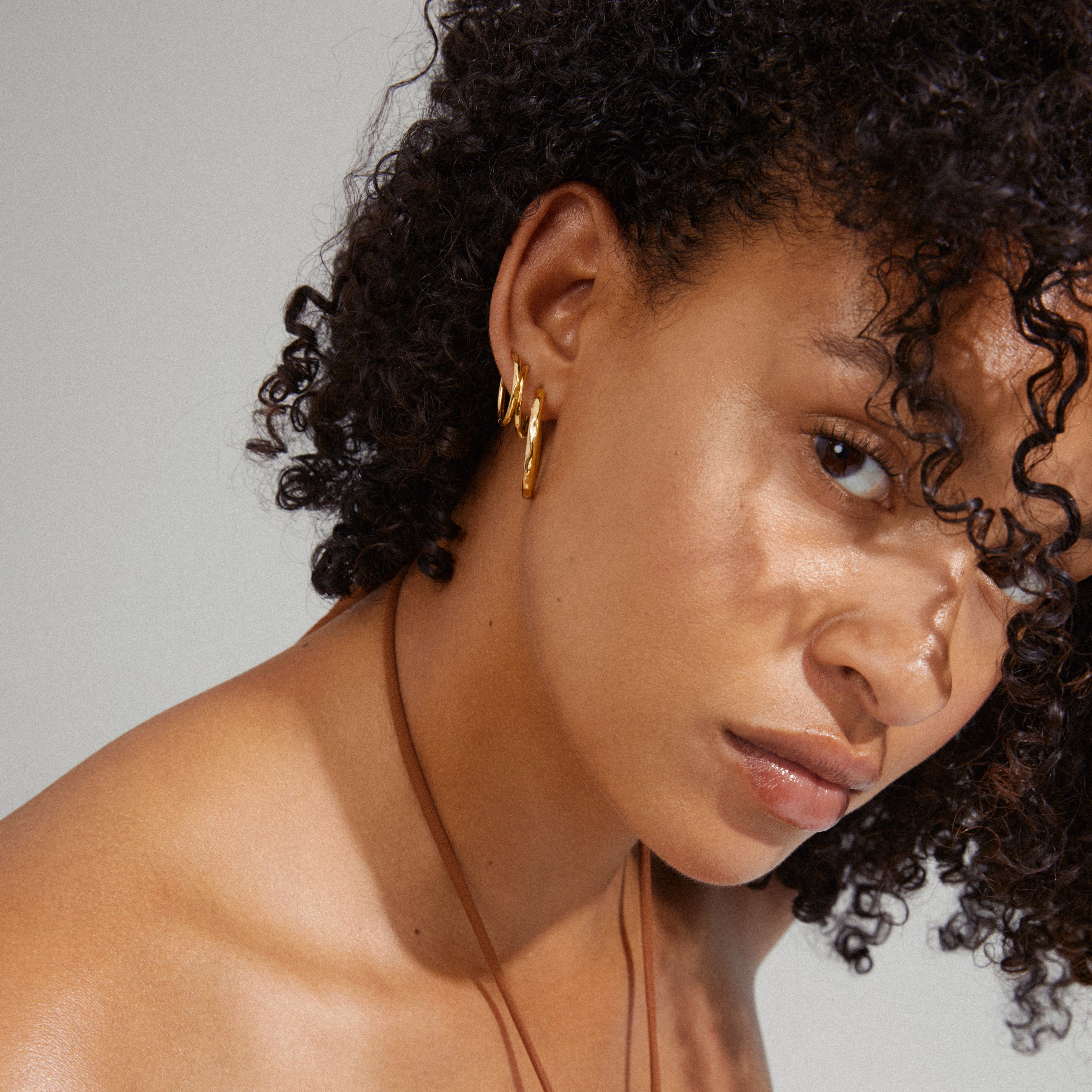 EVE hoop earrings 2-in-1 set gold-plated, worn by a woman with curly hair and a necklace, showcasing elegant, stackable design for a personalized style.