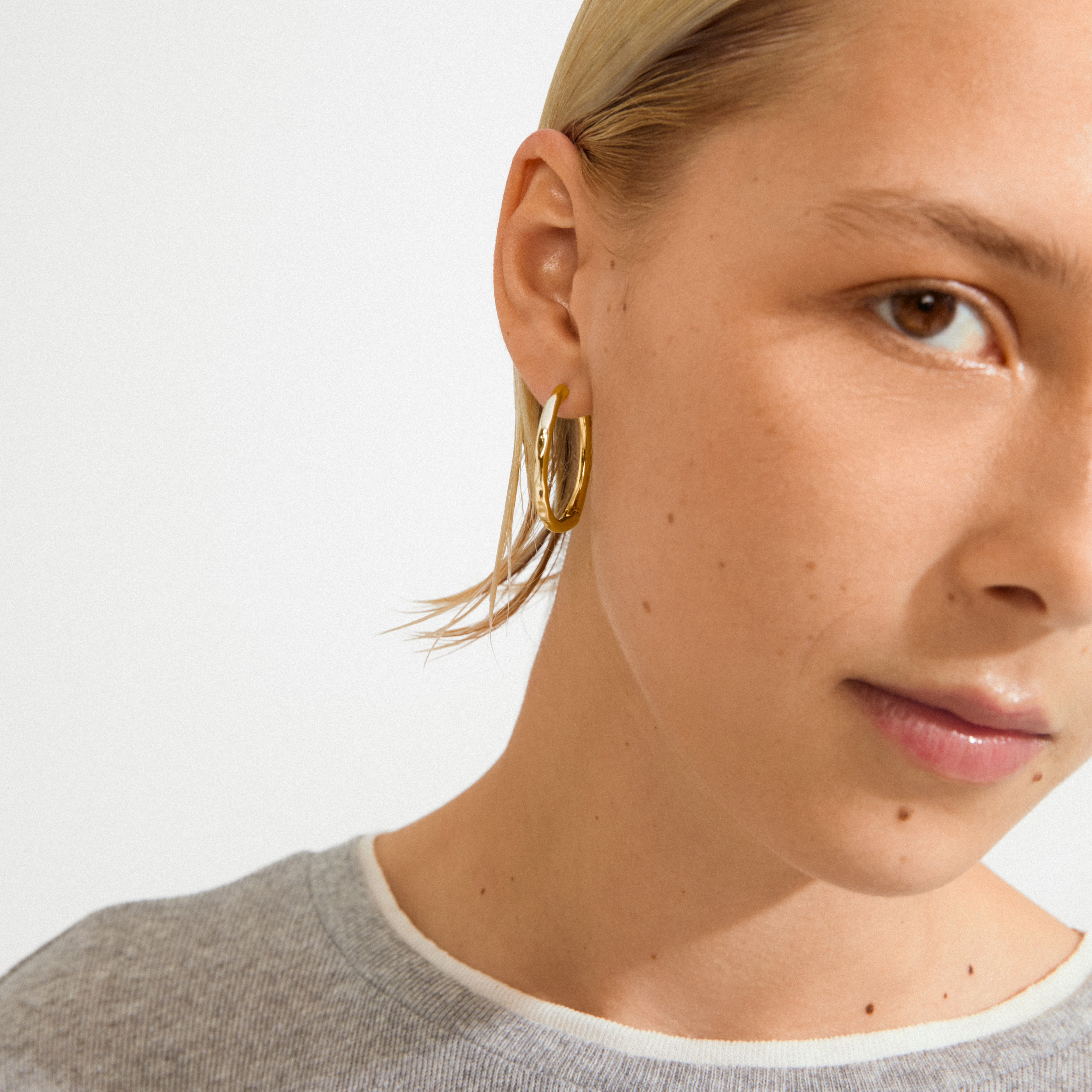 Close-up of a young person wearing Pilgrim's EVE hoop earrings 2-in-1 set, showcasing a simple gold hoop on the earlobe against a soft, natural backdrop.