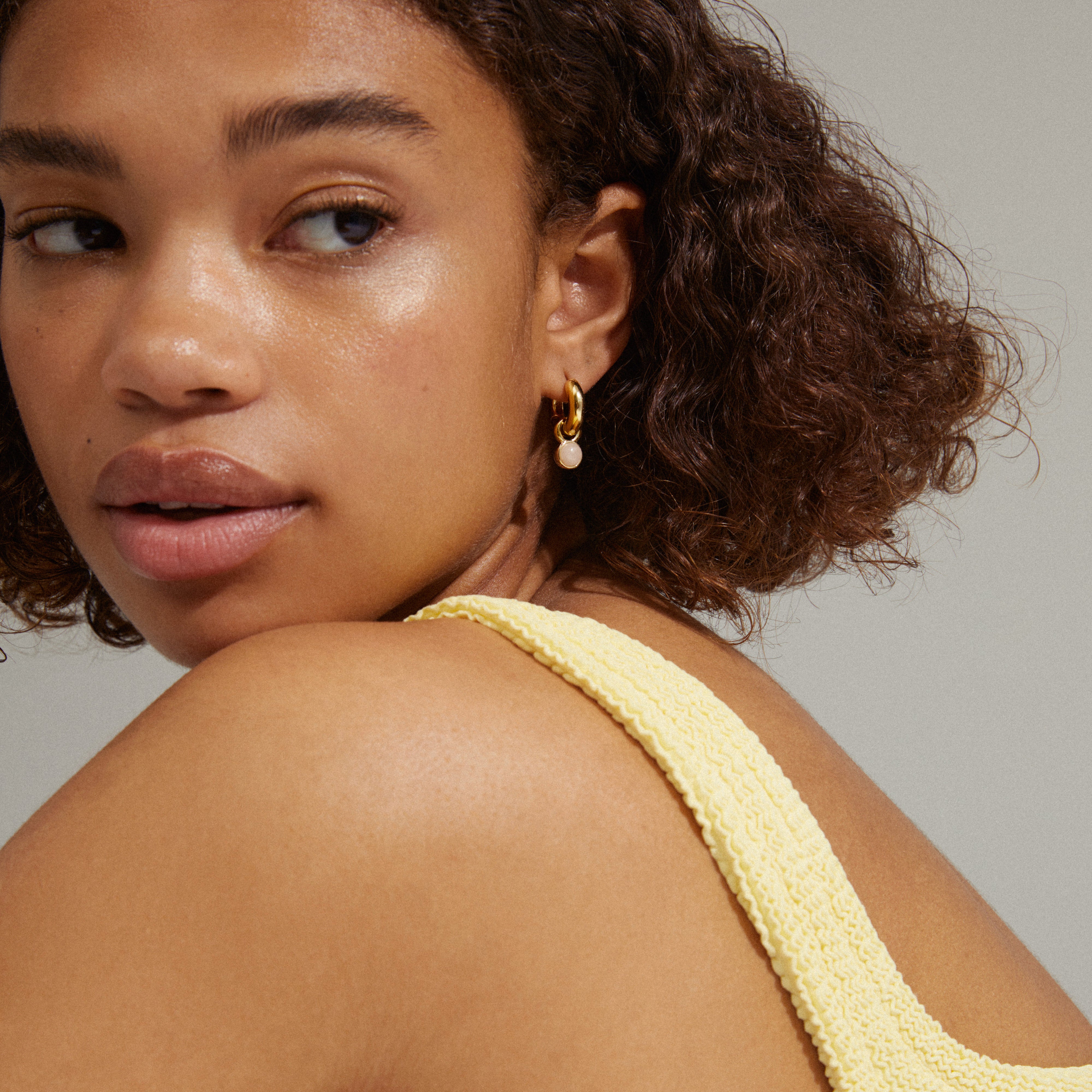 Woman wearing EVAH rosa gold-plated hoop earrings with rose quartz pendants, showcasing their chic and positive energy-enhancing design.