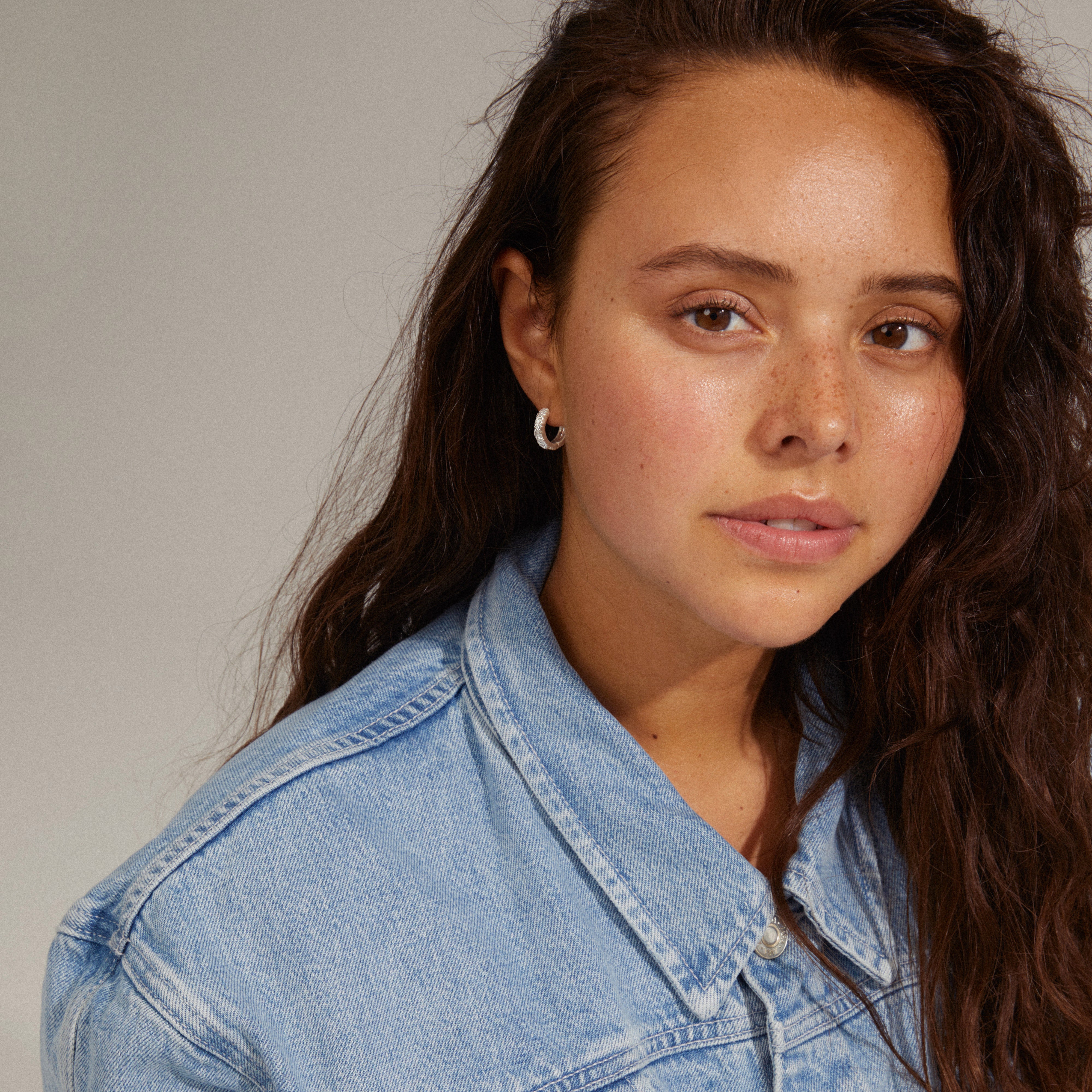 ELFRIDA hoop earrings silver-plated on a woman with long brown hair wearing a denim jacket, showcasing intricate nature-inspired carvings.
