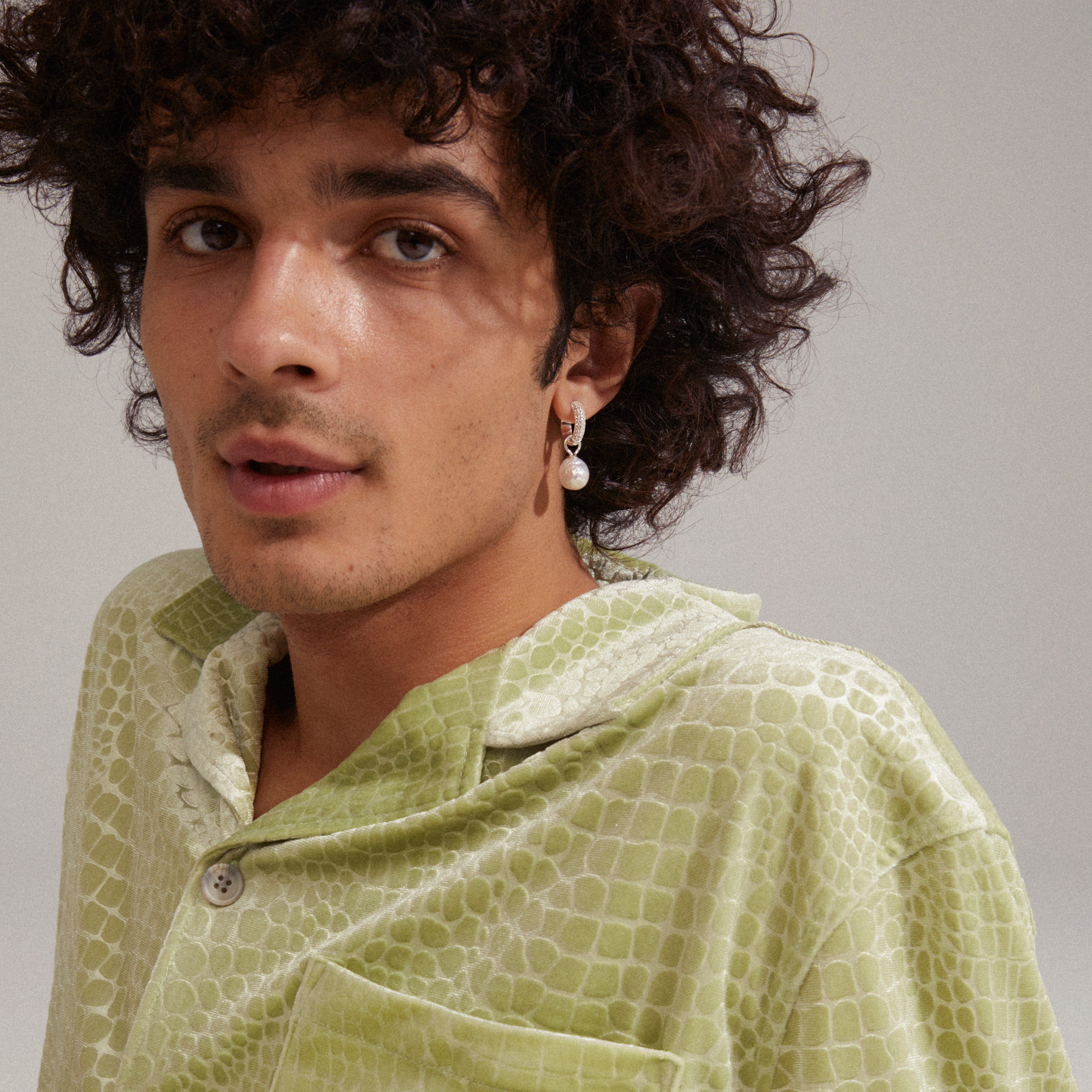 Man with curly hair wearing EDELE pearl earrings silver-plated by Pilgrim, featuring chunky hoops with Preciosa crystals, styled for a trendy, glamorous look.