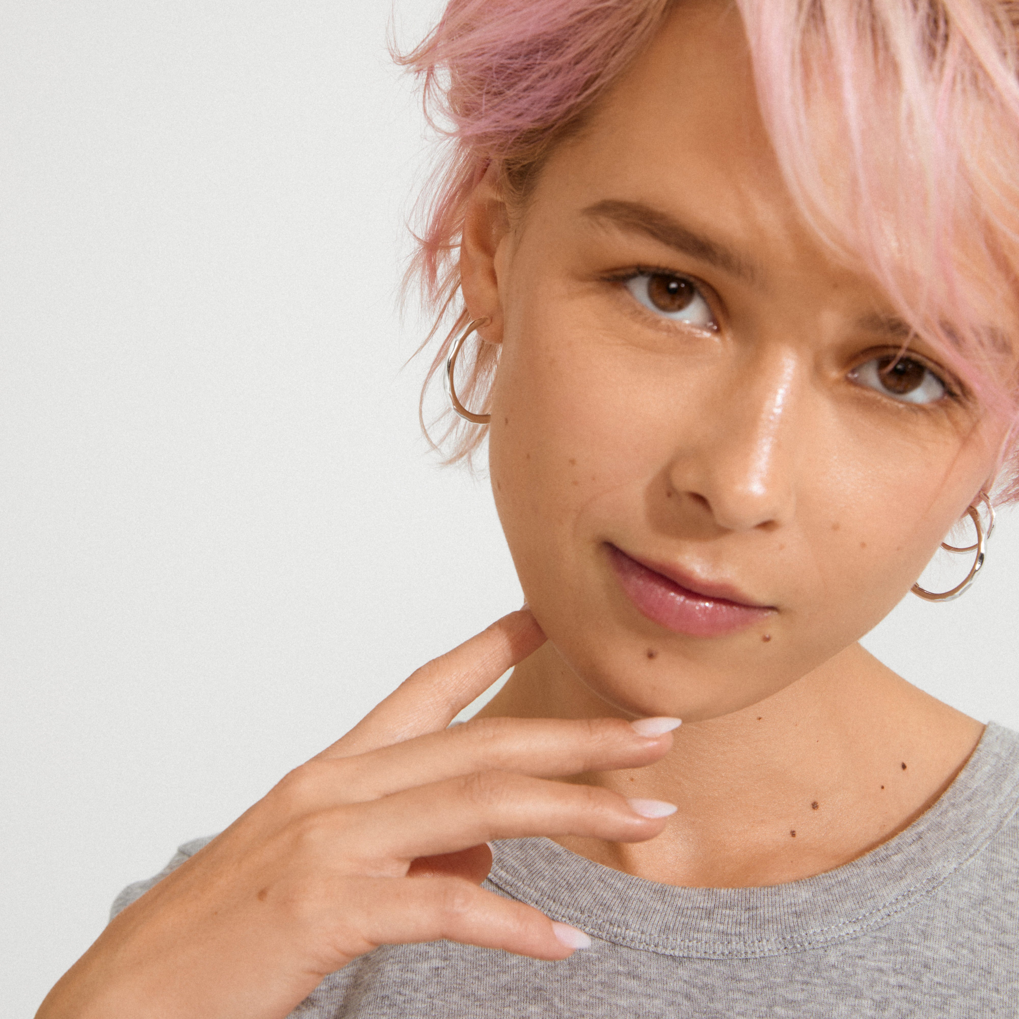 Young person with pastel-pink hair wearing Pilgrim's EVE hoop earrings 2-in-1 set, showcasing a minimalist style with silver-plated hoops for a personalized look.