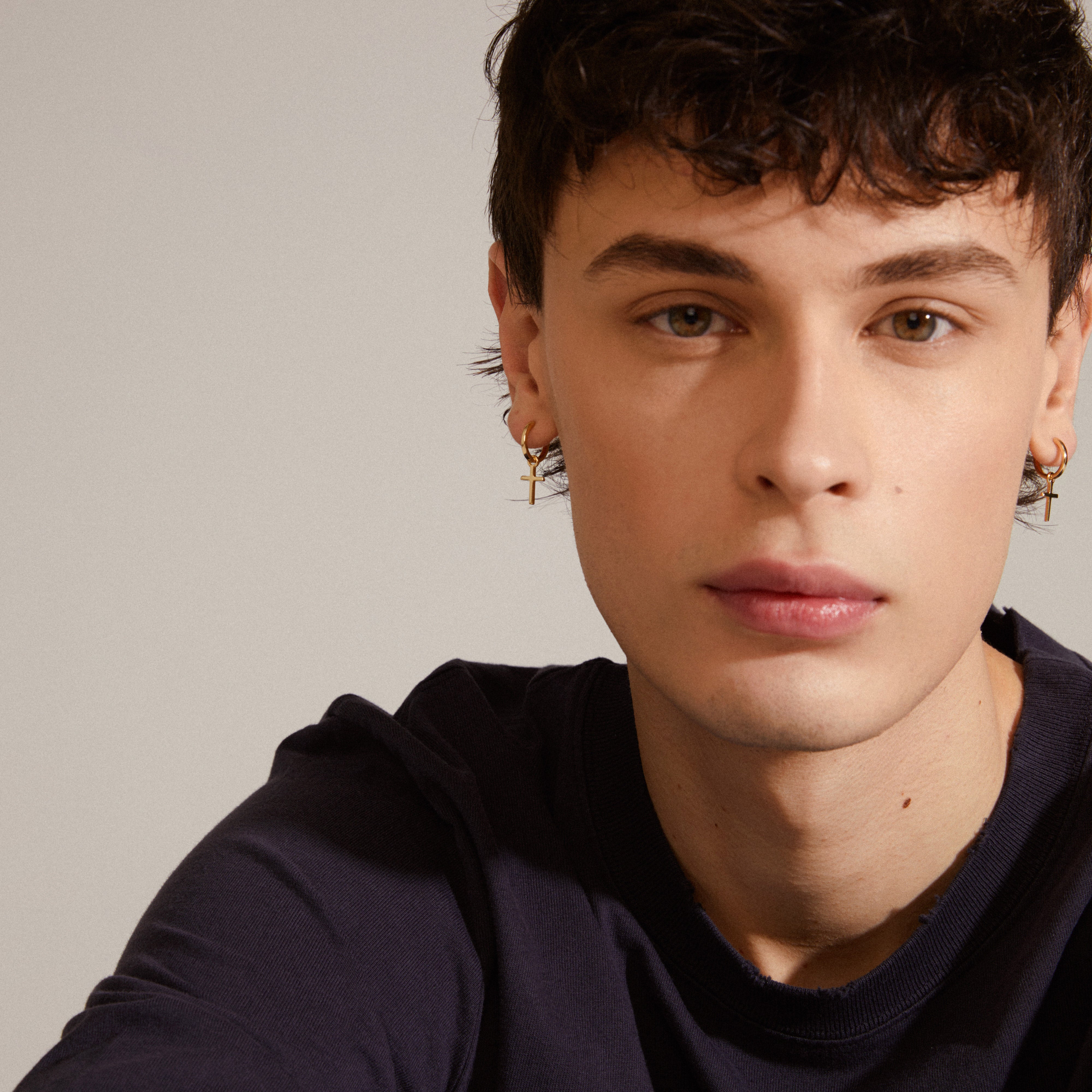 DAISY cross hoops gold-plated earrings, featuring simple huggie hoops with a removable cross pendant, worn by a man taking a selfie.