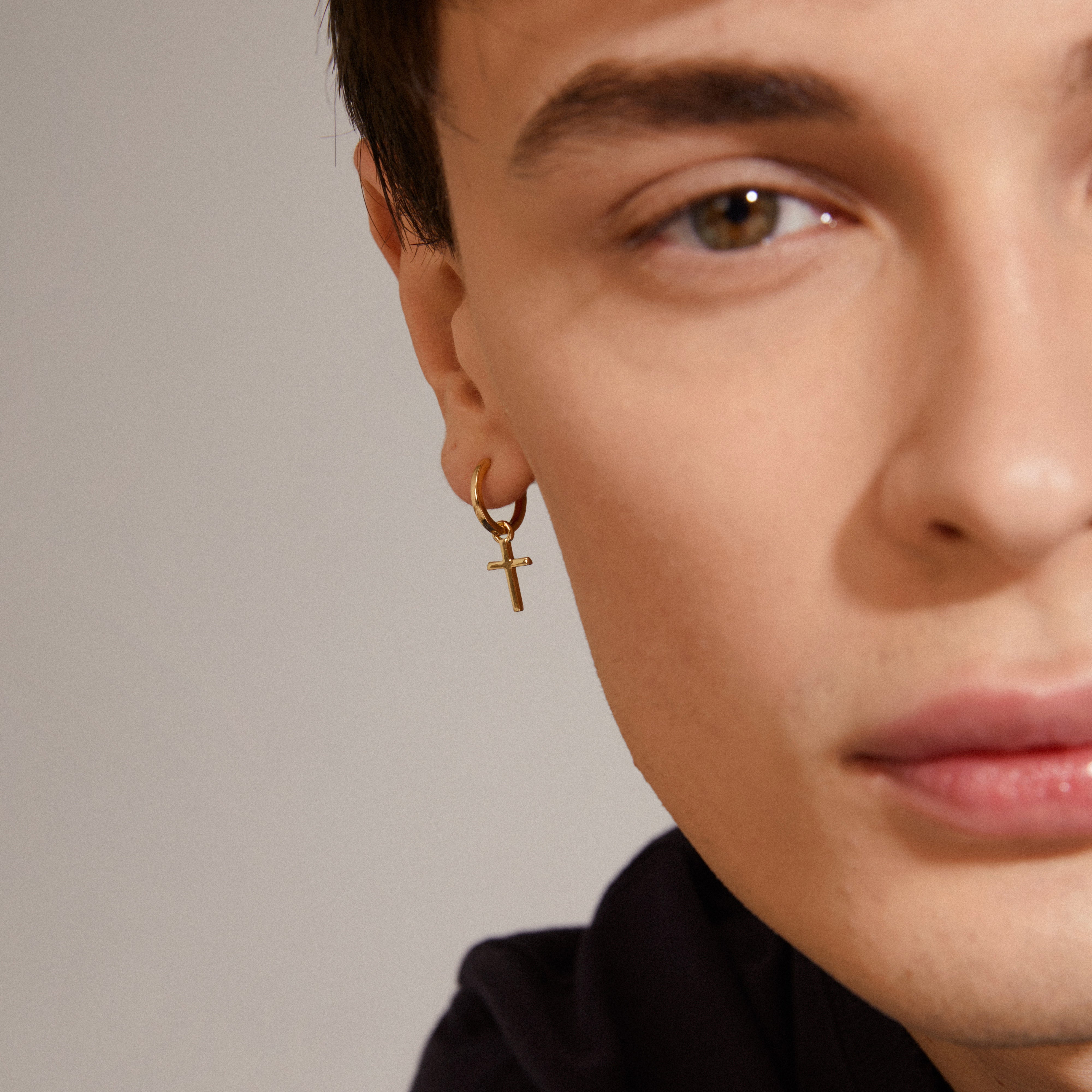 DAISY cross hoops gold-plated: Close-up of a man's face wearing gold-plated huggie hoops with a removable cross pendant from Pilgrim's DAISY collection.