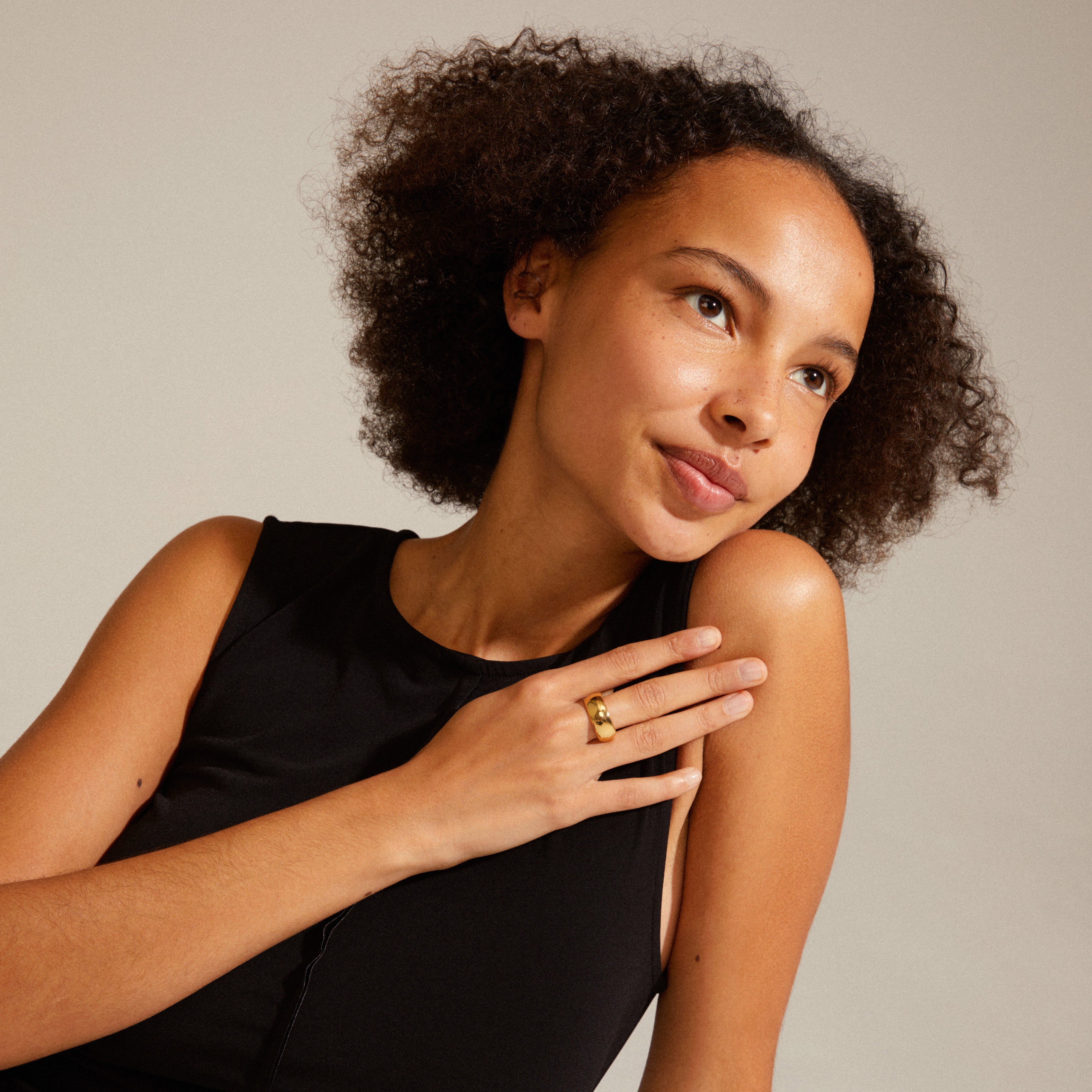 Woman in a black dress wearing the DAISY gold-plated ring by Pilgrim, showcasing its elegant Nordic design and recycled material composition.
