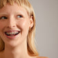 Dominique gold-plated hoop earrings with a unique square snake design and shiny details, worn by a smiling woman showcasing braces.