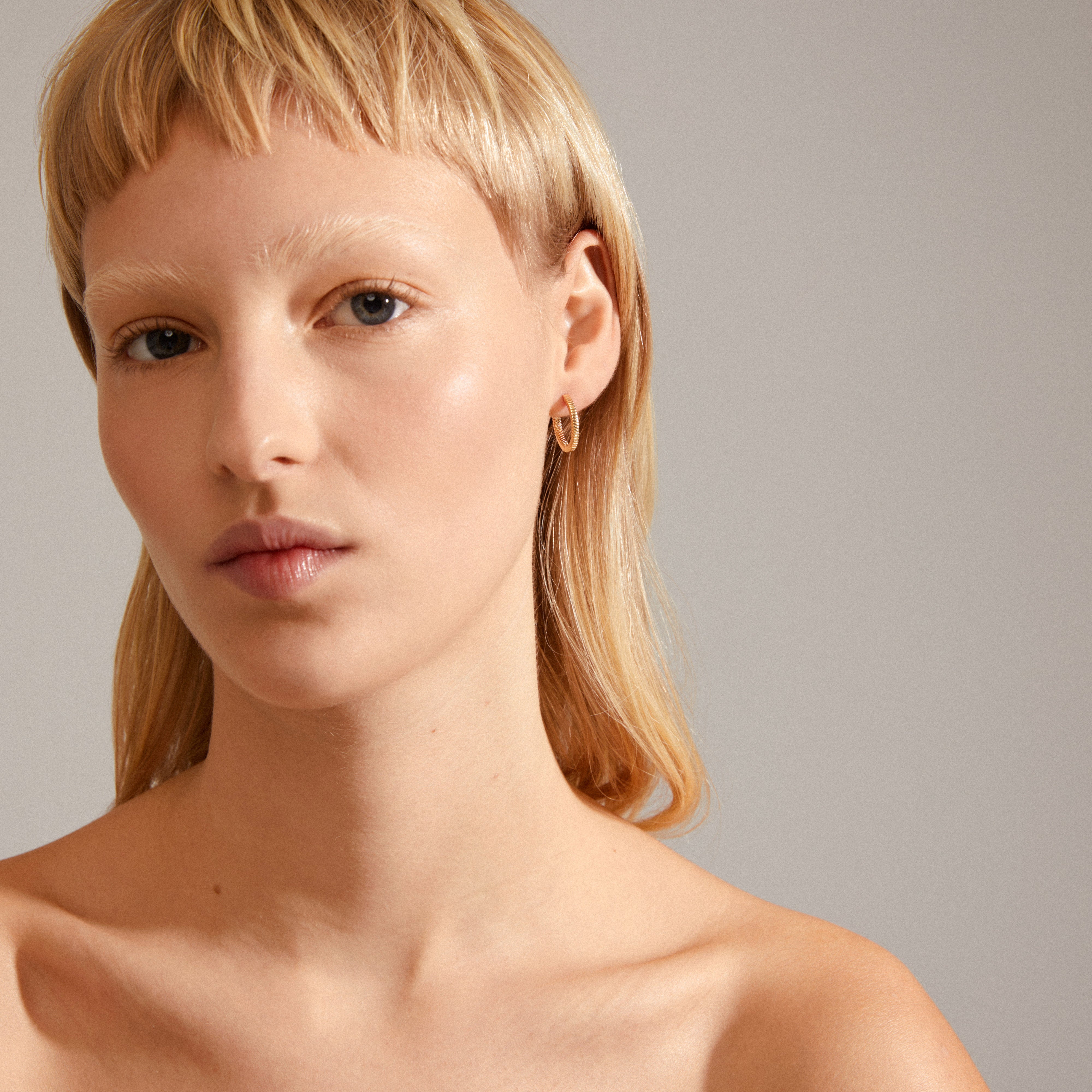 Close-up of a woman wearing DOMINIQUE gold-plated hoop earrings with a unique square snake design, highlighting their shiny details and easy click lock mechanism.