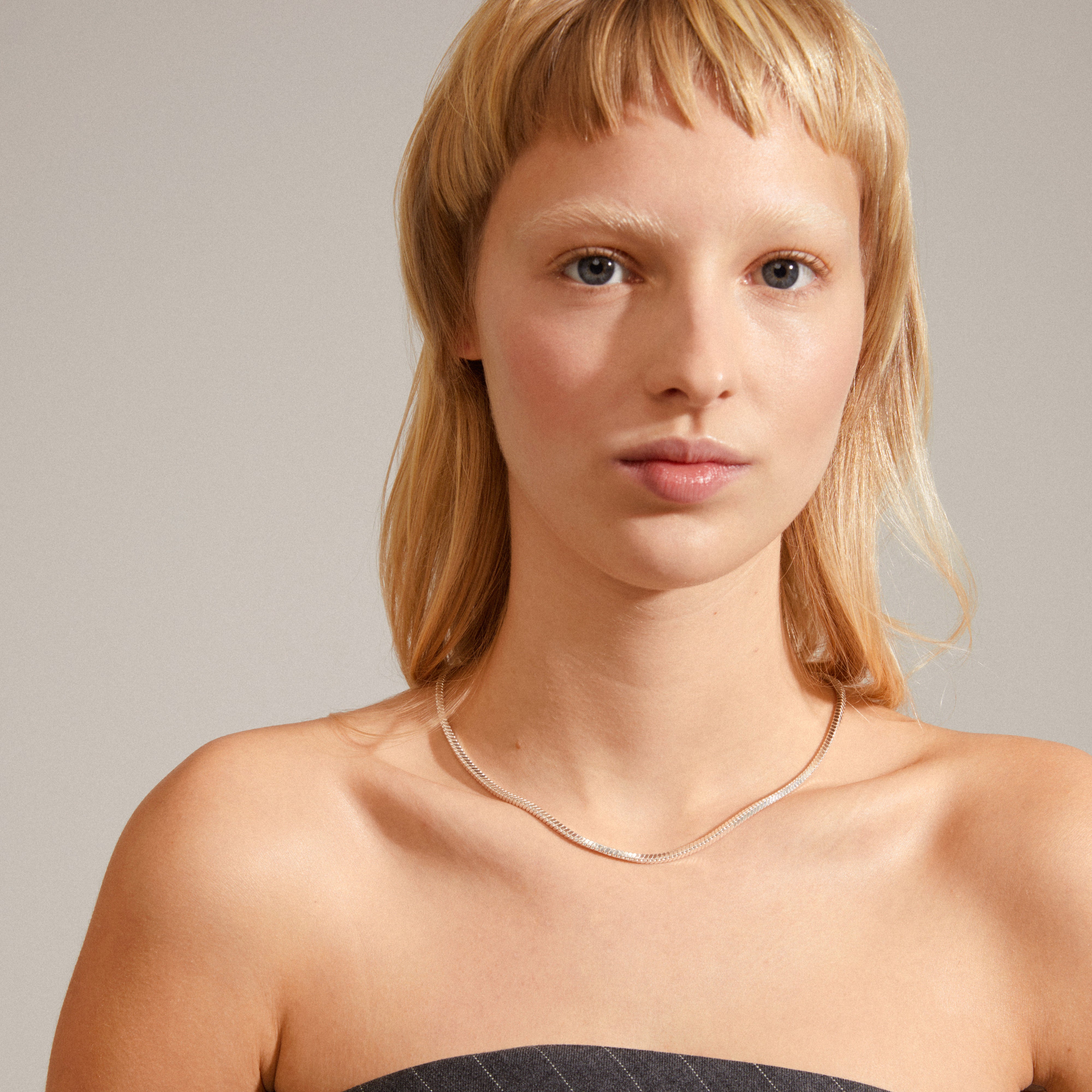 Woman wearing the DOMINIQUE necklace, a silver-plated, square snake chain by Pilgrim, showcased in a close-up portrait highlighting its shine and soft shapes.