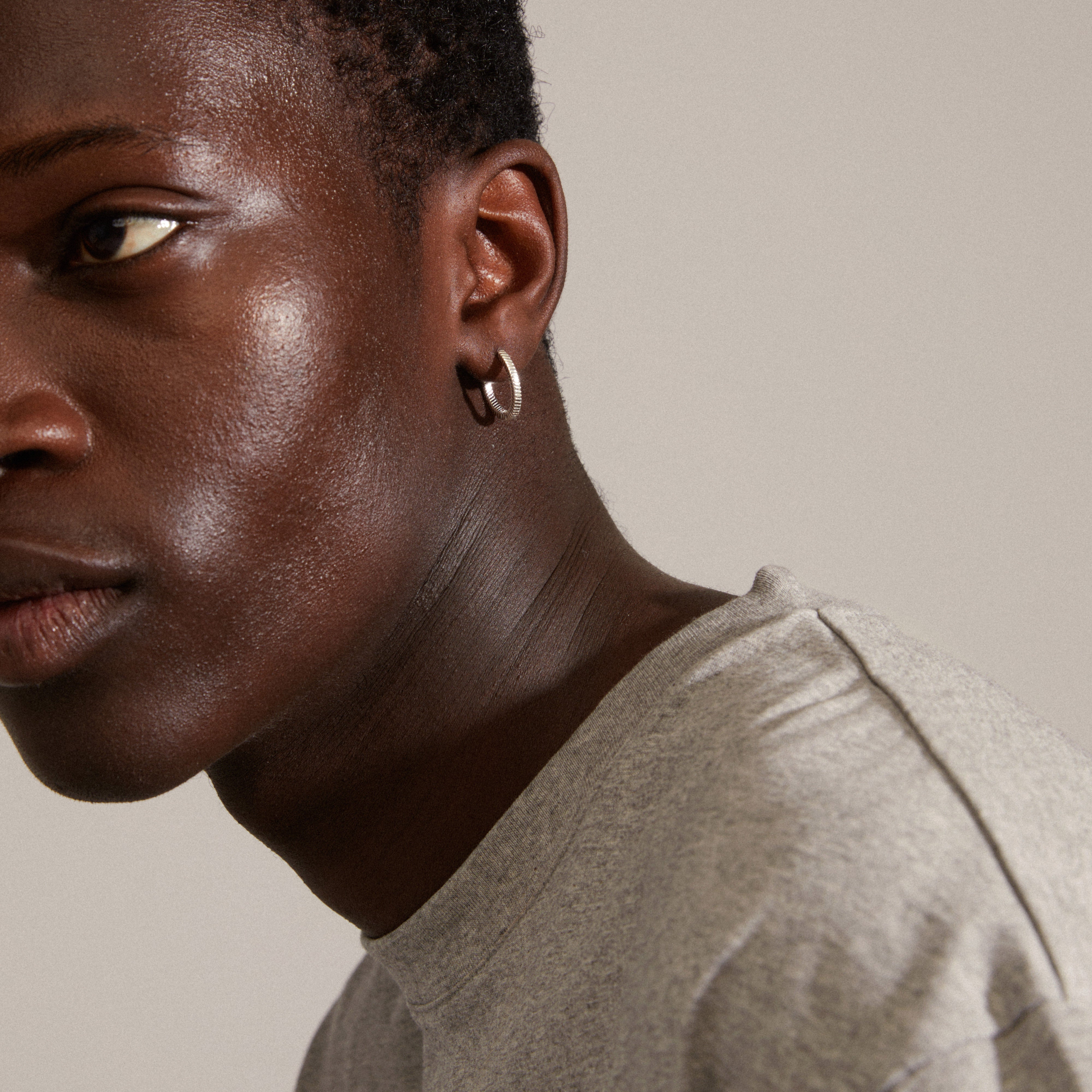 Silver-plated DOMINIQUE hoop earrings with a unique square snake design, showcasing intricate patterns and shine, worn by a person with short hair.