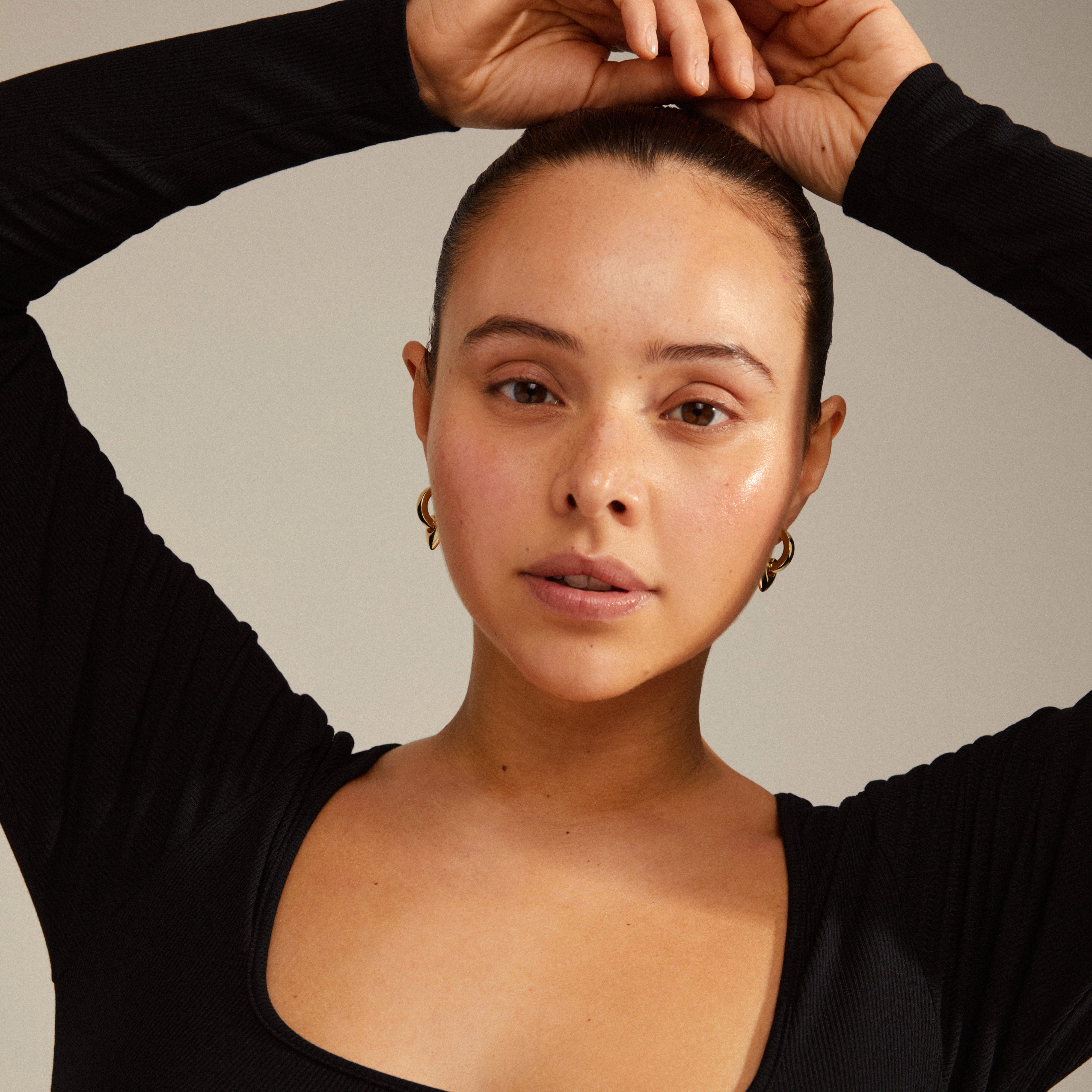 Woman with hand on head showcasing Pilgrim's IOKASTE chunky hoops gold-plated earrings, featuring detachable heart pendants and easy click lock design.