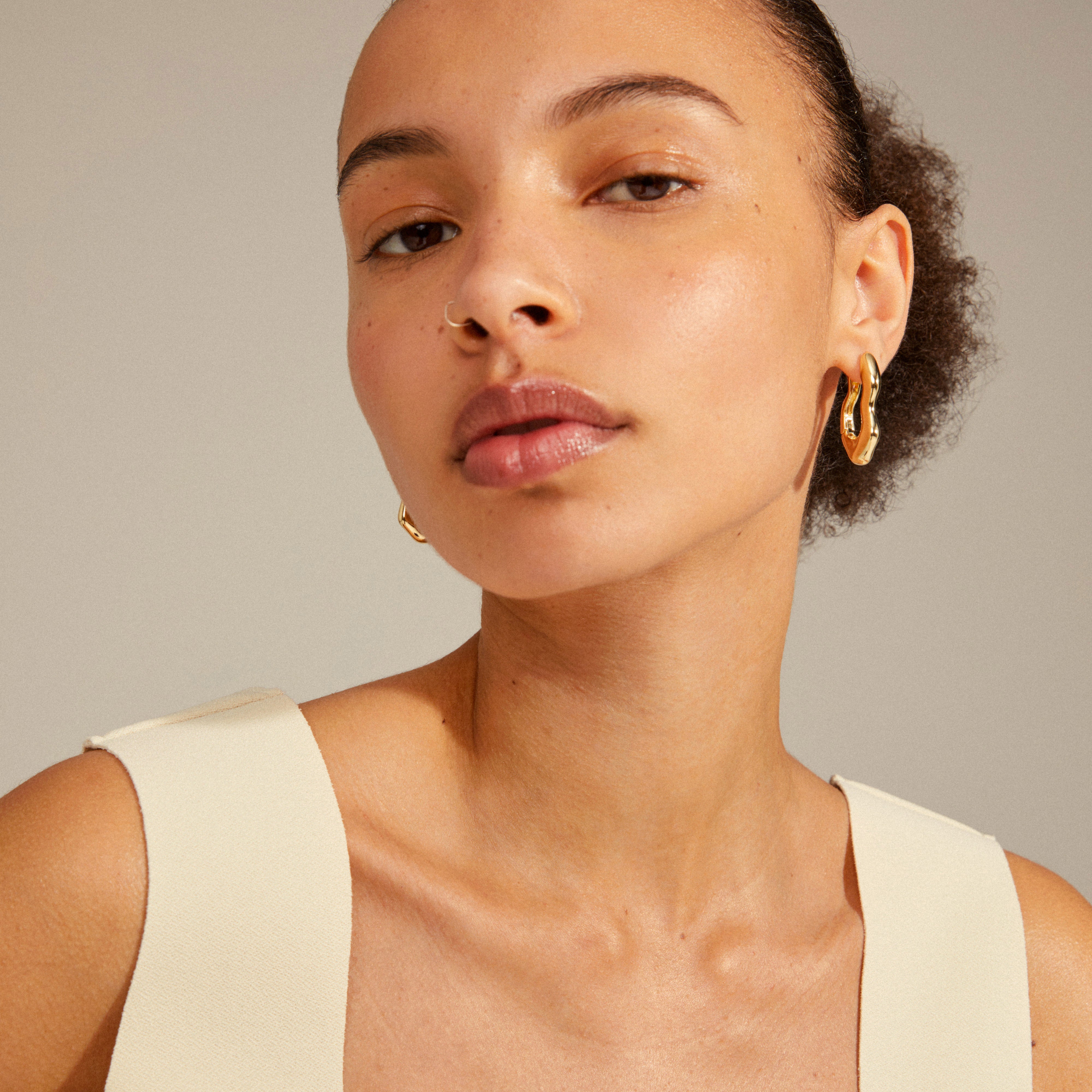 LOULIA wavy earrings gold-plated on a woman; oblong hoops with organic silhouette, shiny finish, click clasp, emphasizing style and trend.