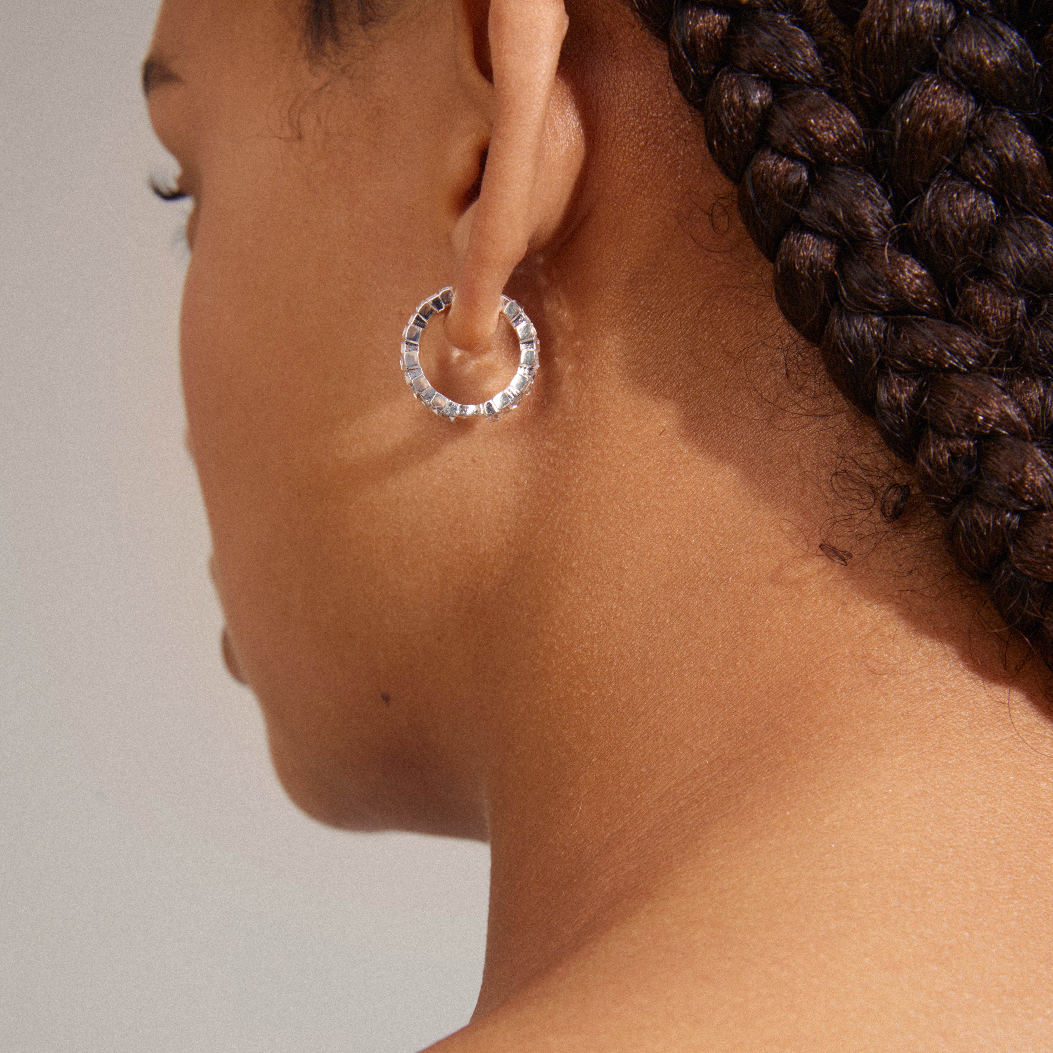 Close-up of a woman wearing Pilgrim's HELI crystal hoop earrings, silver-plated with staggered light crystals, showcasing a sophisticated and modern design.