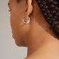 Close-up of a woman wearing Pilgrim's HELI crystal hoop earrings, silver-plated with staggered light crystals, showcasing a sophisticated and modern design.