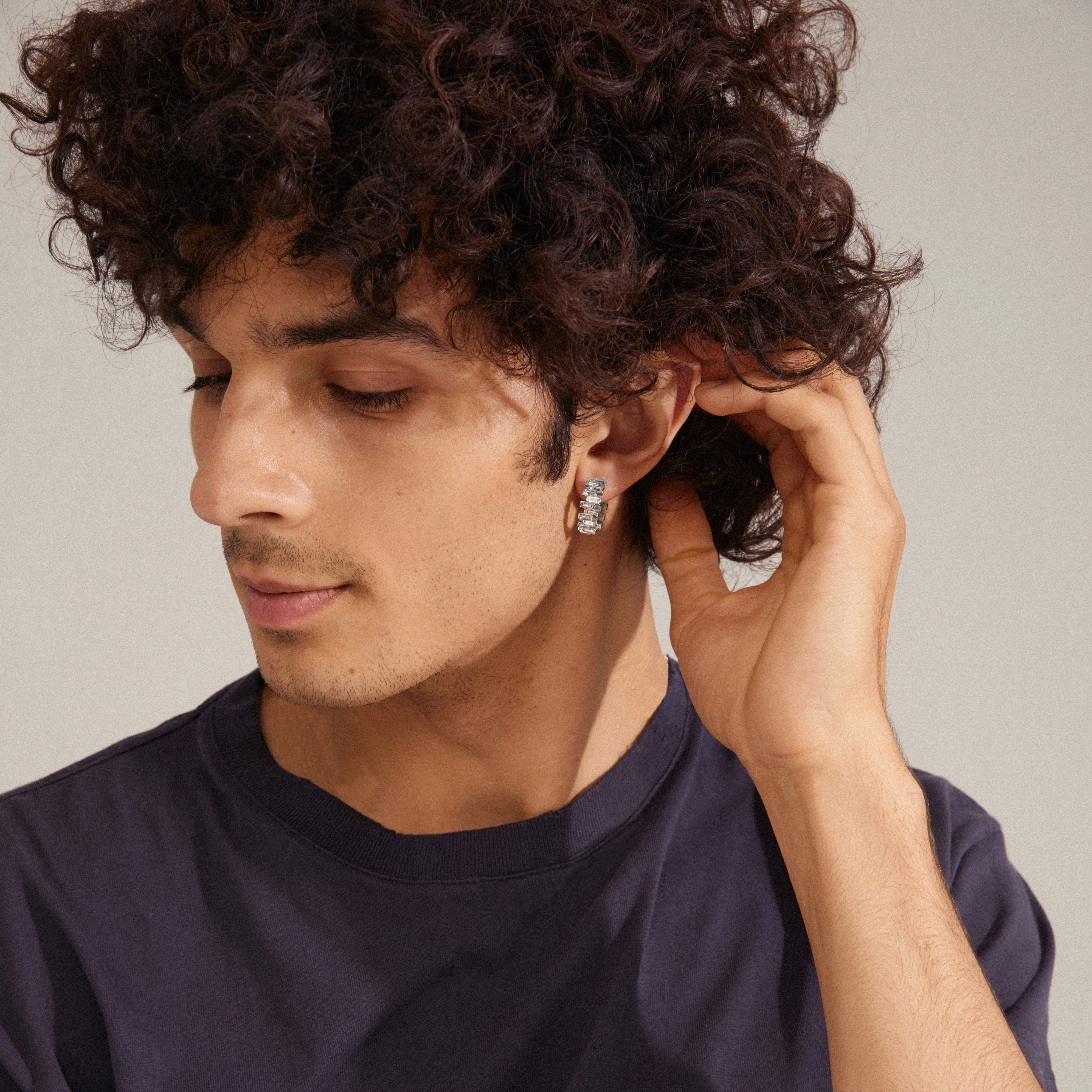 Man wearing Pilgrim's HELI crystal hoop earrings, silver-plated with staggered light crystal stones, highlighting the earrings' eye-catching structure and classy vibe.