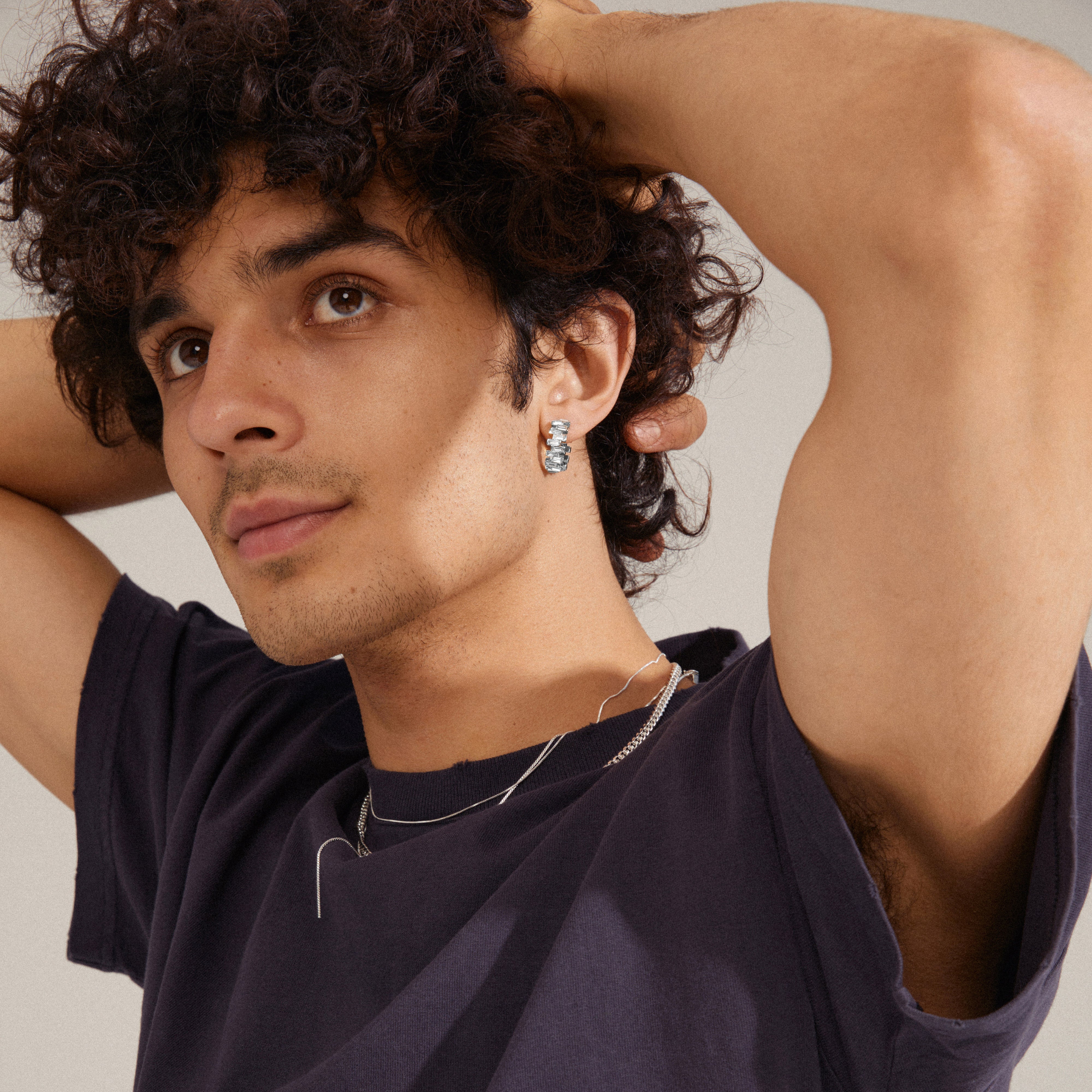 HELI crystal hoop earrings, silver-plated, featuring staggered light crystal stones, worn by a man with curly hair and earrings for a classy, trendy look.