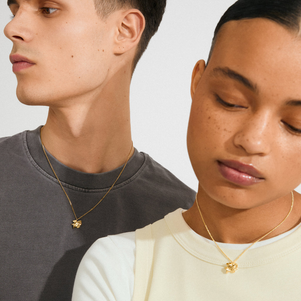 Two young adults wearing Pilgrim's gold-plated TIMBER necklaces with organic flower pendants, showcasing minimalist, adjustable designs ideal for layering and personal style.