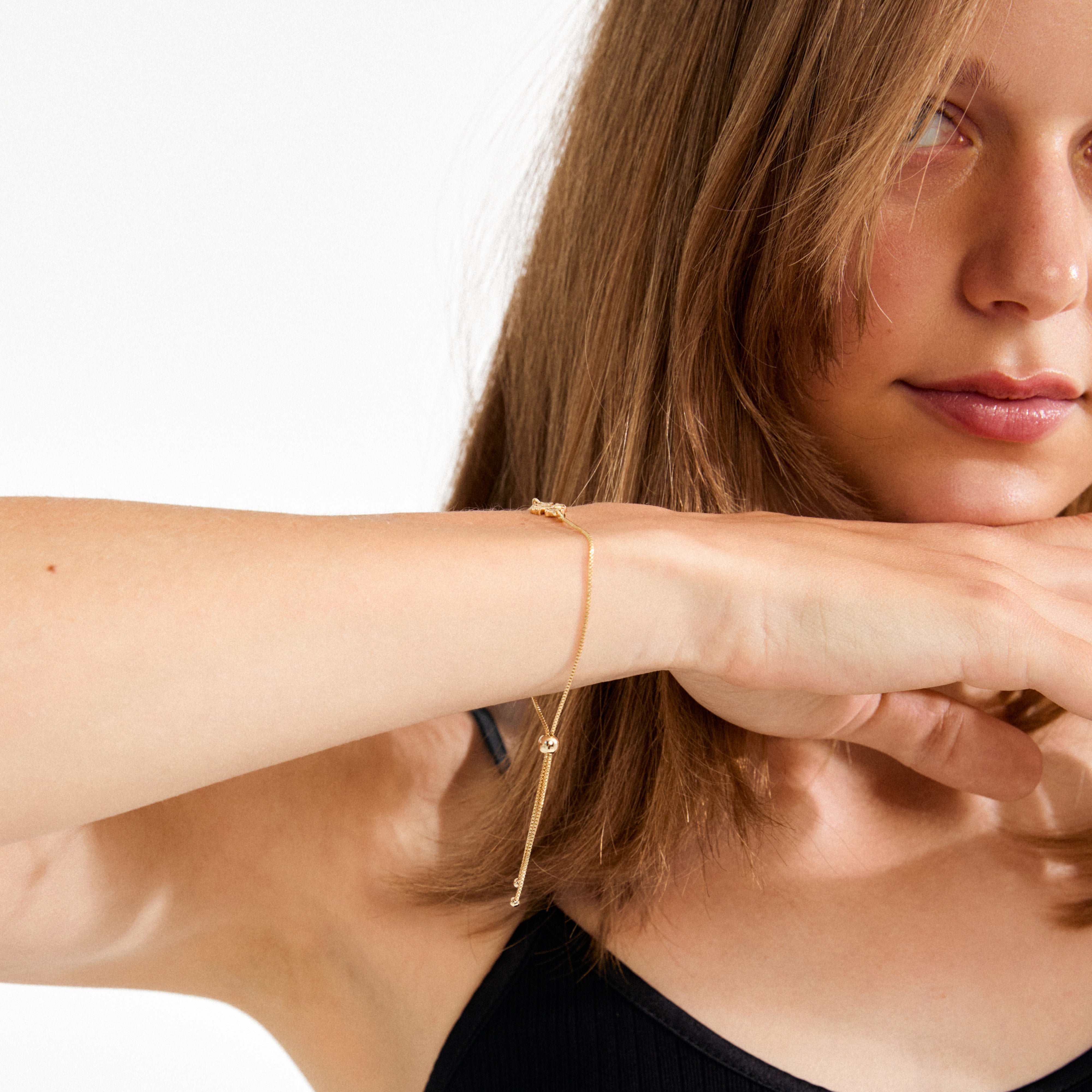 Young woman showcases the DAGMAR gold-plated bracelet by Pilgrim, featuring a delicate adjustable chain with a small cross pendant, reflecting timeless Danish elegance.