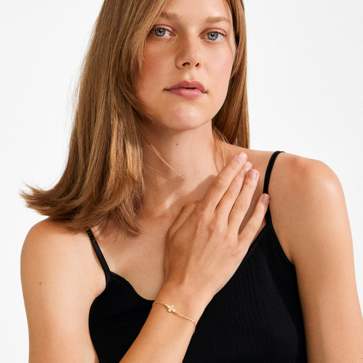 Young woman wearing a DAGMAR bracelet, gold-plated, featuring a delicate chain and cross pendant, highlighting minimalist, timeless Danish design and craftsmanship.