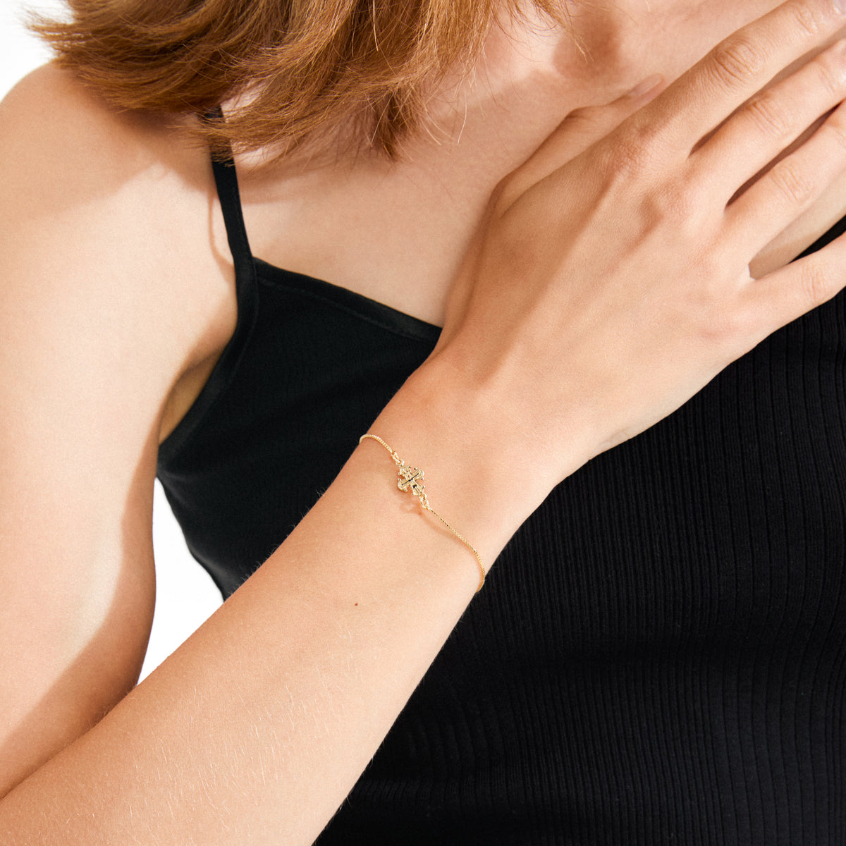 Woman wearing DAGMAR bracelet gold-plated, featuring a delicate gold chain with a flower-like cross charm, resting on her wrist against her collarbone.