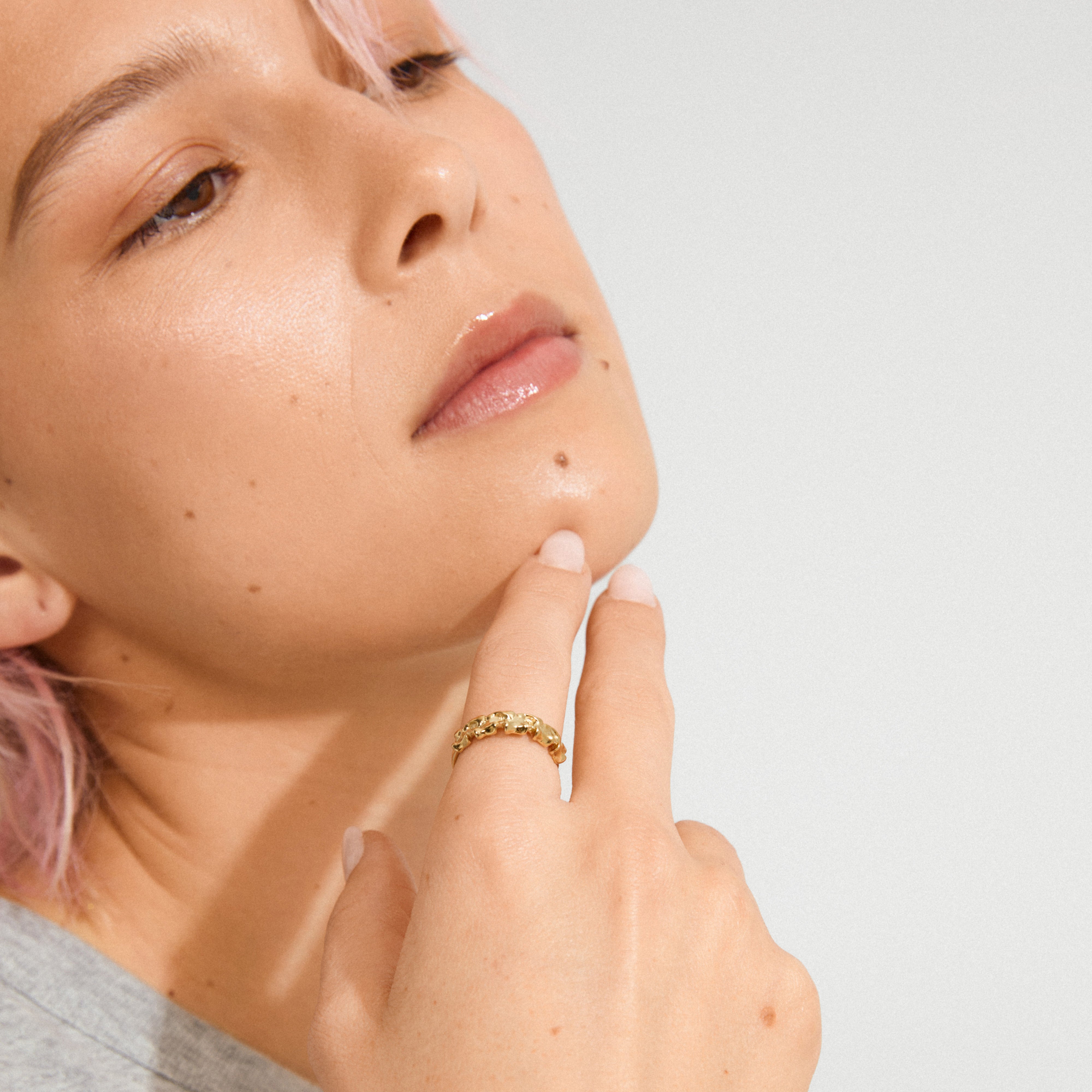 Close-up of a person's hand under their chin, showcasing the gold-plated TIMBER ring by Pilgrim, featuring abstract floral details, reflecting nature-inspired elegance.