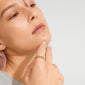 Close-up of a person's hand under their chin, showcasing the gold-plated TIMBER ring by Pilgrim, featuring abstract floral details, reflecting nature-inspired elegance.