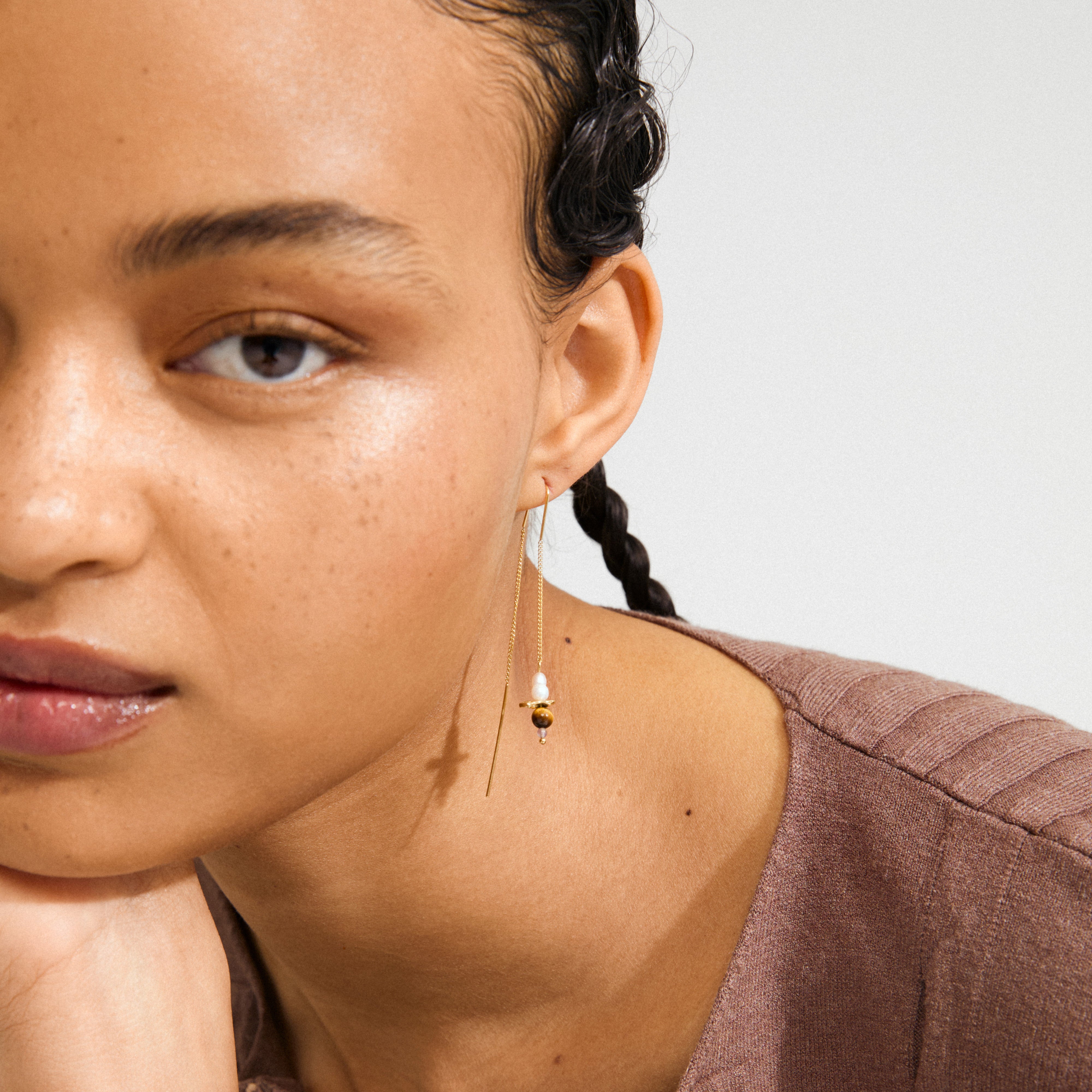 Young person wearing SEQUOIA chain earrings gold-plated with a pearl and gold bead, showcasing a delicate, handcrafted style with a natural, dewy complexion.